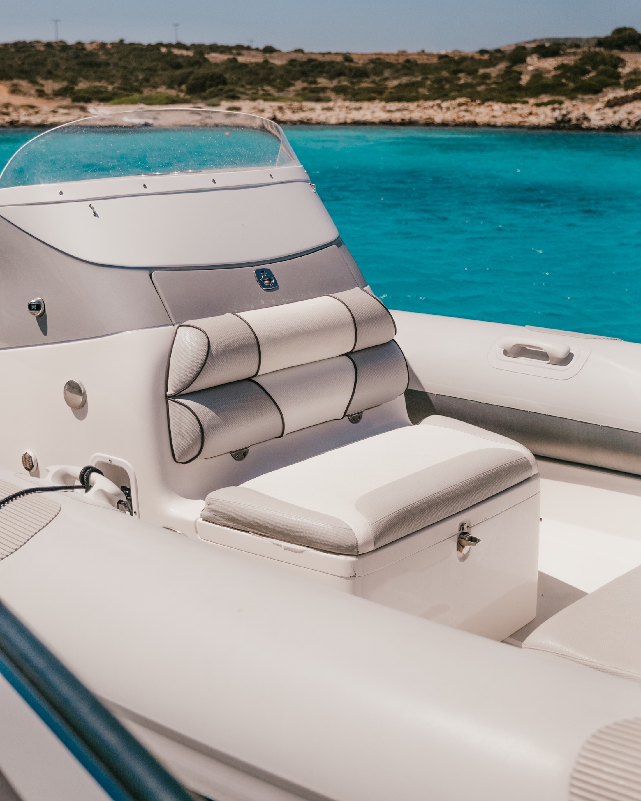 White Rock 36 speedboat with captain at helm cruising calm blue waters near Paros coastline with hills in background.