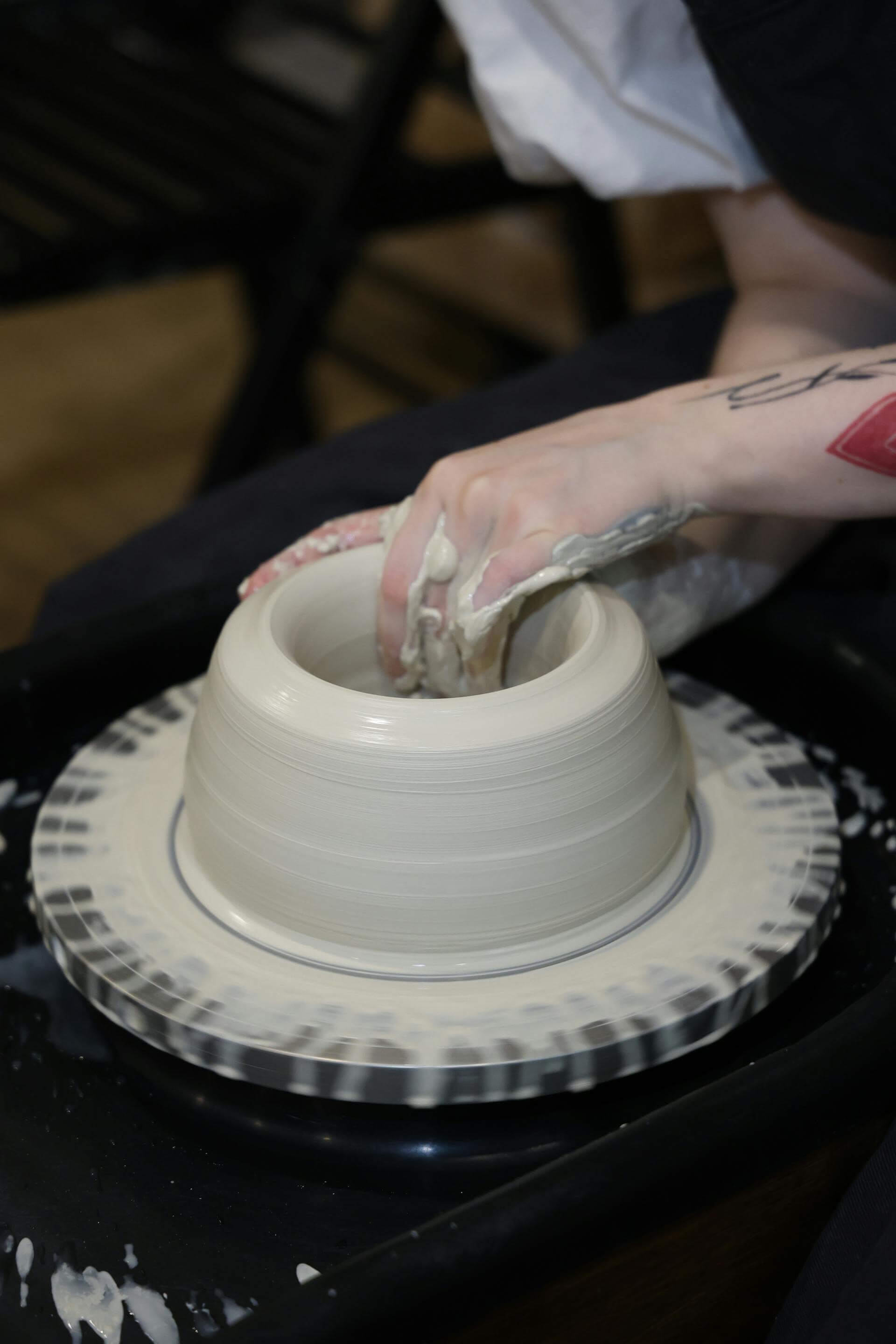 A person skillfully shapes clay into a pot on a spinning potter's wheel, showcasing the art of pottery