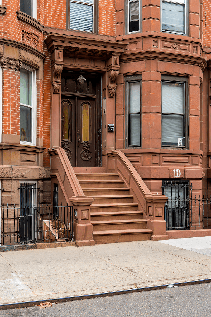Brownstone townhouse entrance with brick facade, raised stoop, ornate wooden door, and black iron railings.