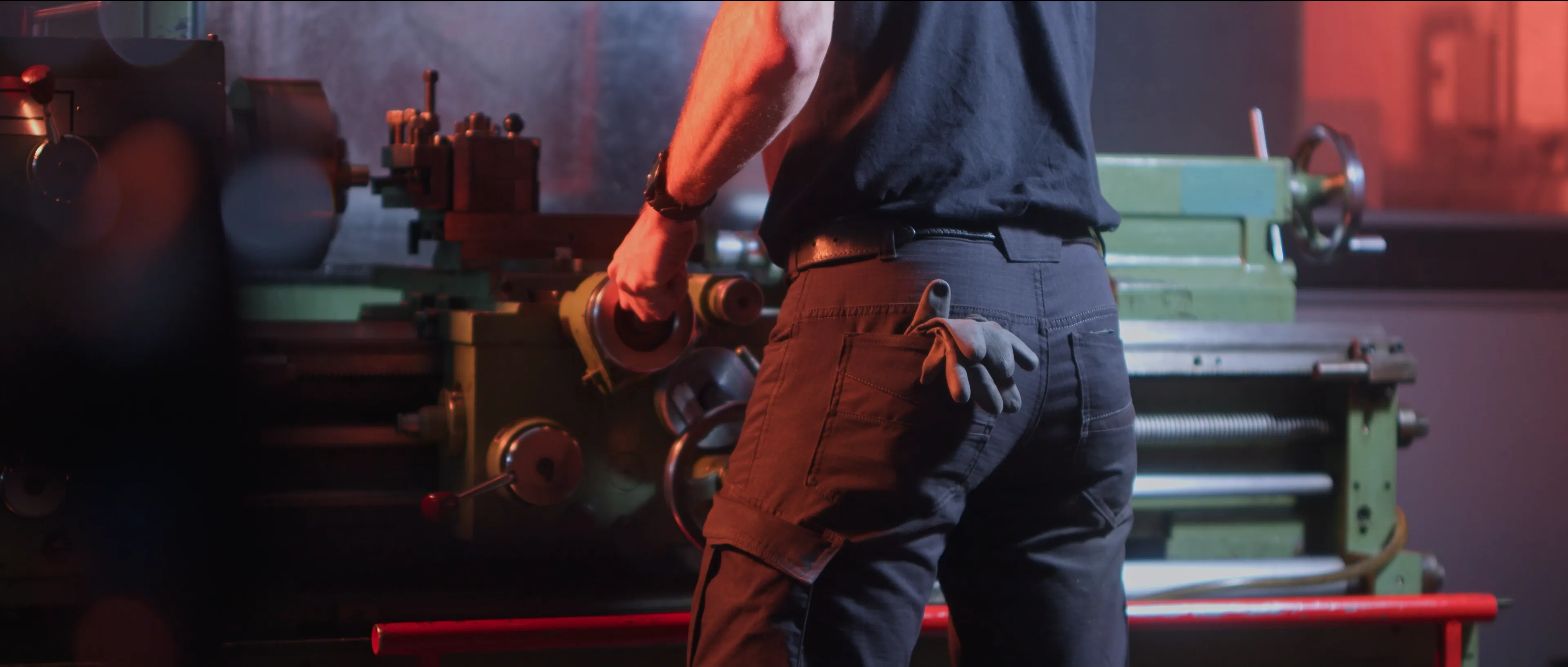 A person operating a vintage industrial lathe in a dimly-lit workshop, highlighting the intricate metalwork and machinery controls.