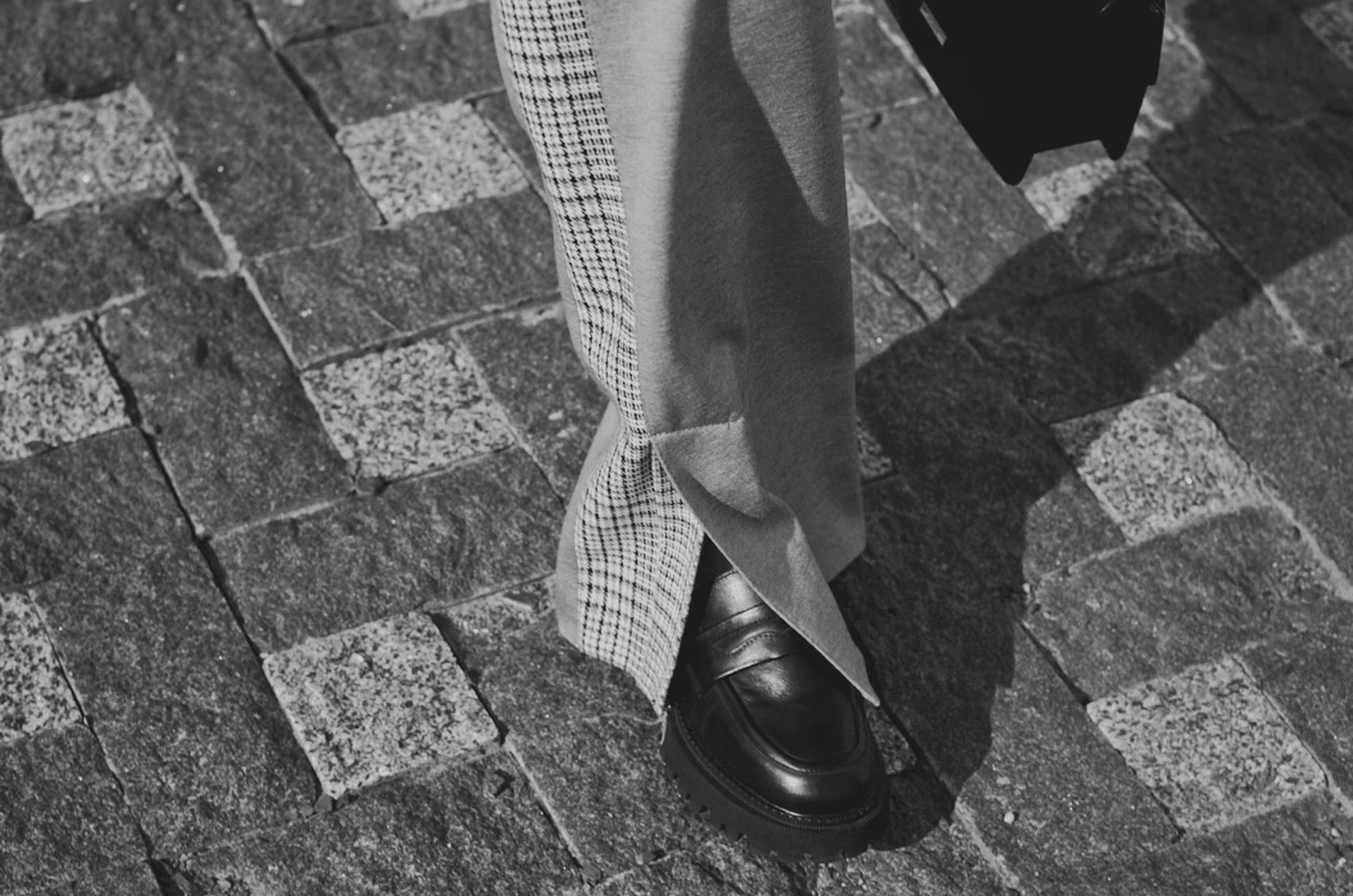 Close-up black-and-white photograph of a professional walking on a cobblestone street in tailored trousers and leather loafers, symbolizing business leadership, account-based selling, and executive decision-making.