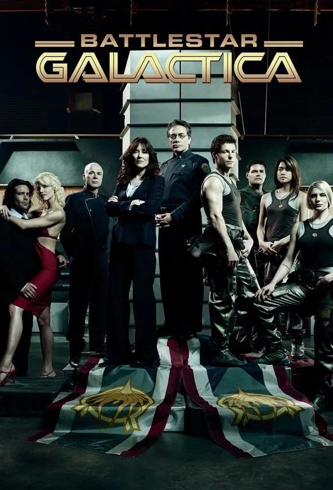 A group of people in futuristic attire stand on a stage adorned with two banners featuring star emblems, set against a dark, industrial background, with "Battlestar Galactica" prominently displayed above.