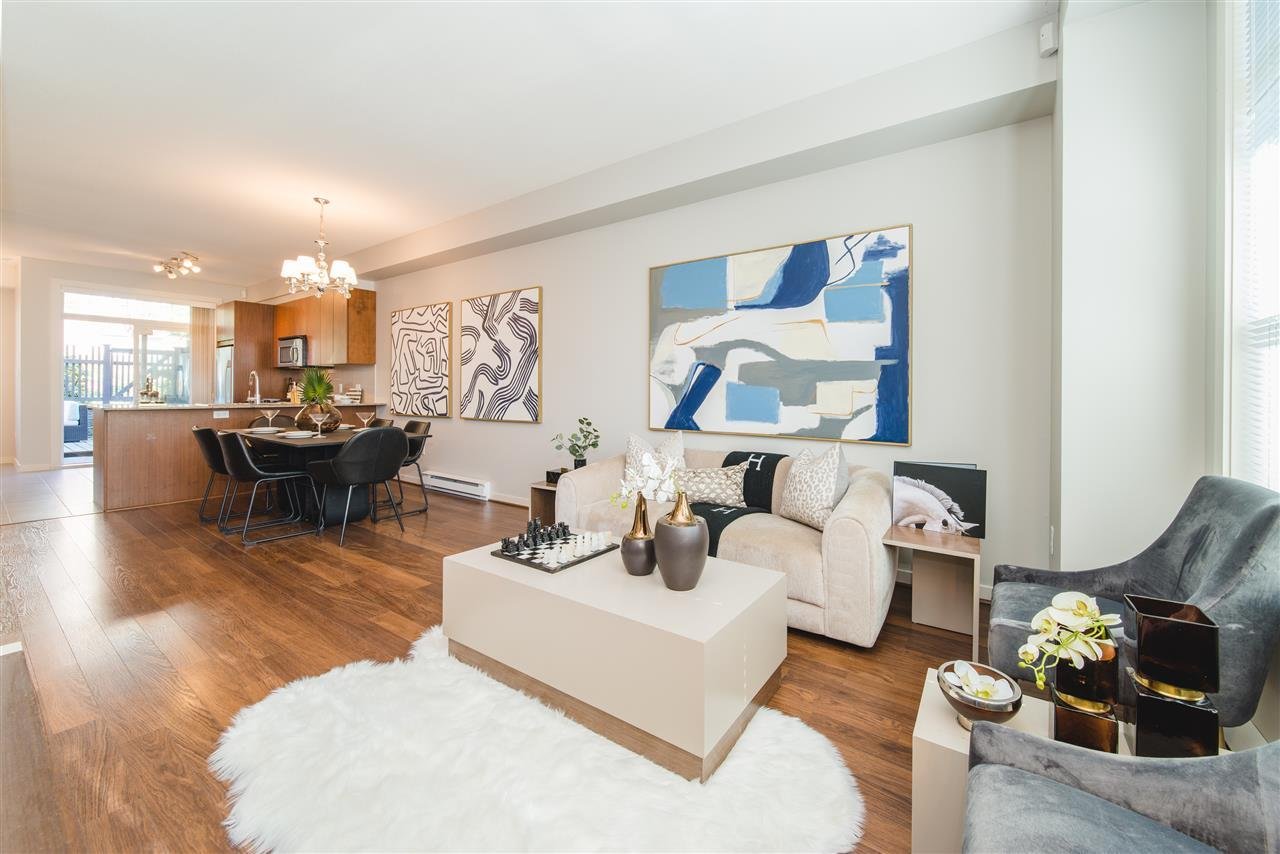 A modern living room featuring neutral furniture, hardwood floors, and abstract artwork on the walls.