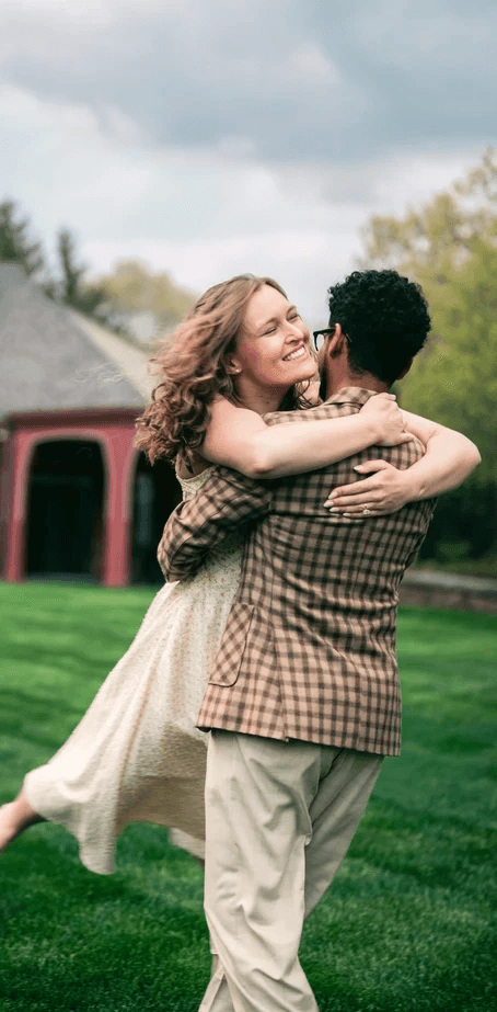 A couple dances closely, showcasing a flowing green dress, against a soft, blurred background of other guests.