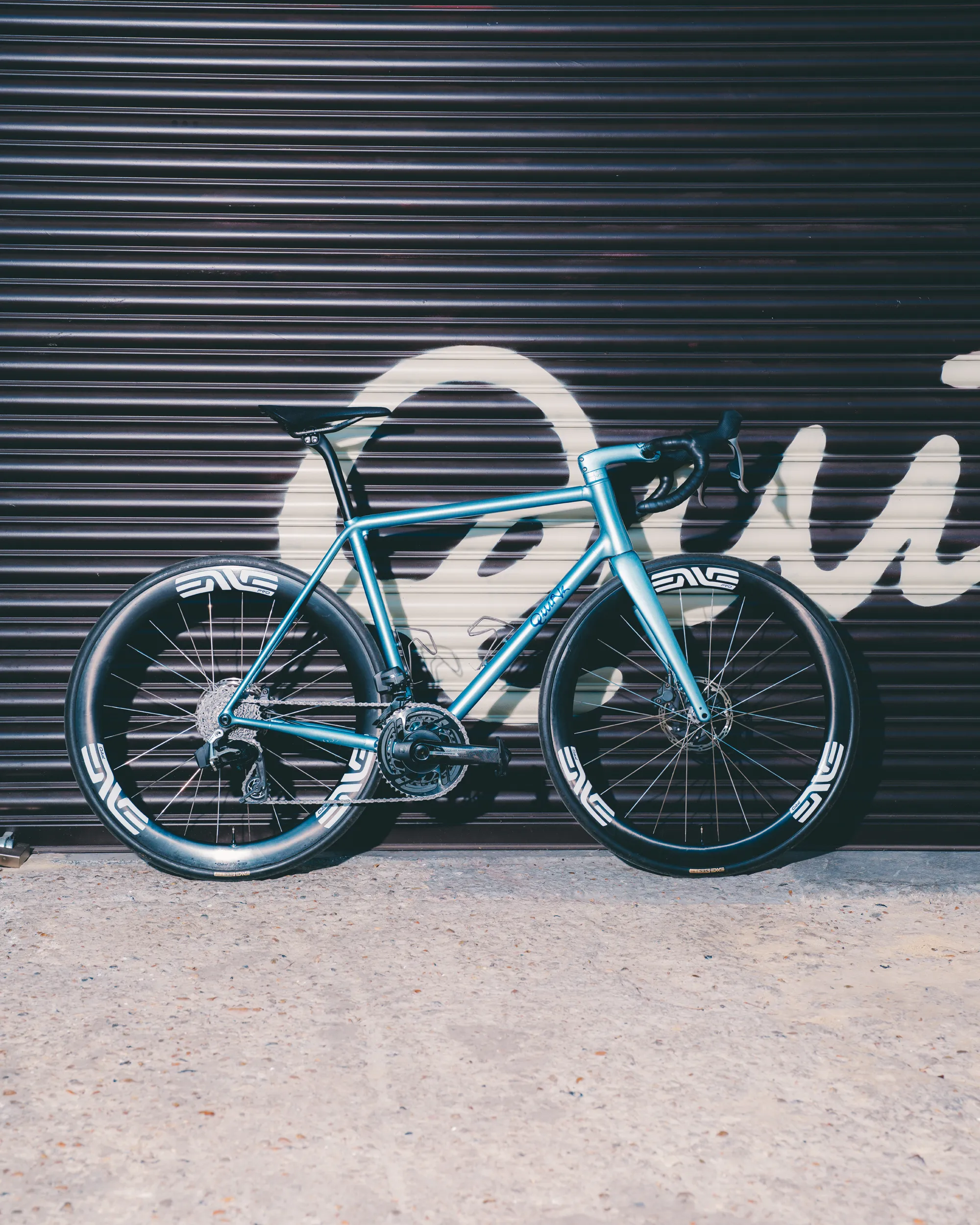 Light blue Quirk Cycles Durmitor road bike in a workshop with dark wheels
