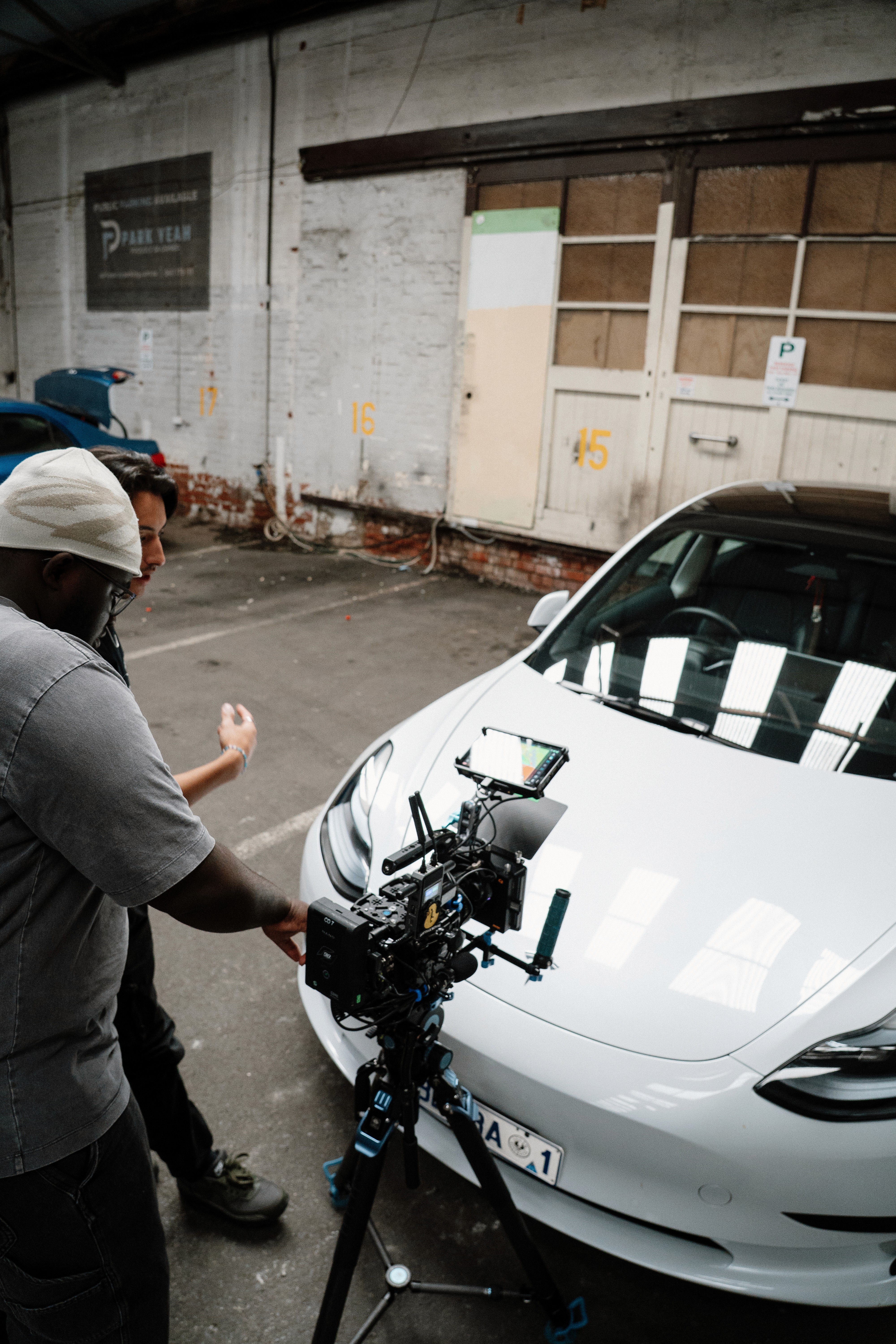 Two filmmakers operate a large camera on a dimly lit set. One wears headphones, both focused, suggesting a serious, creative atmosphere.