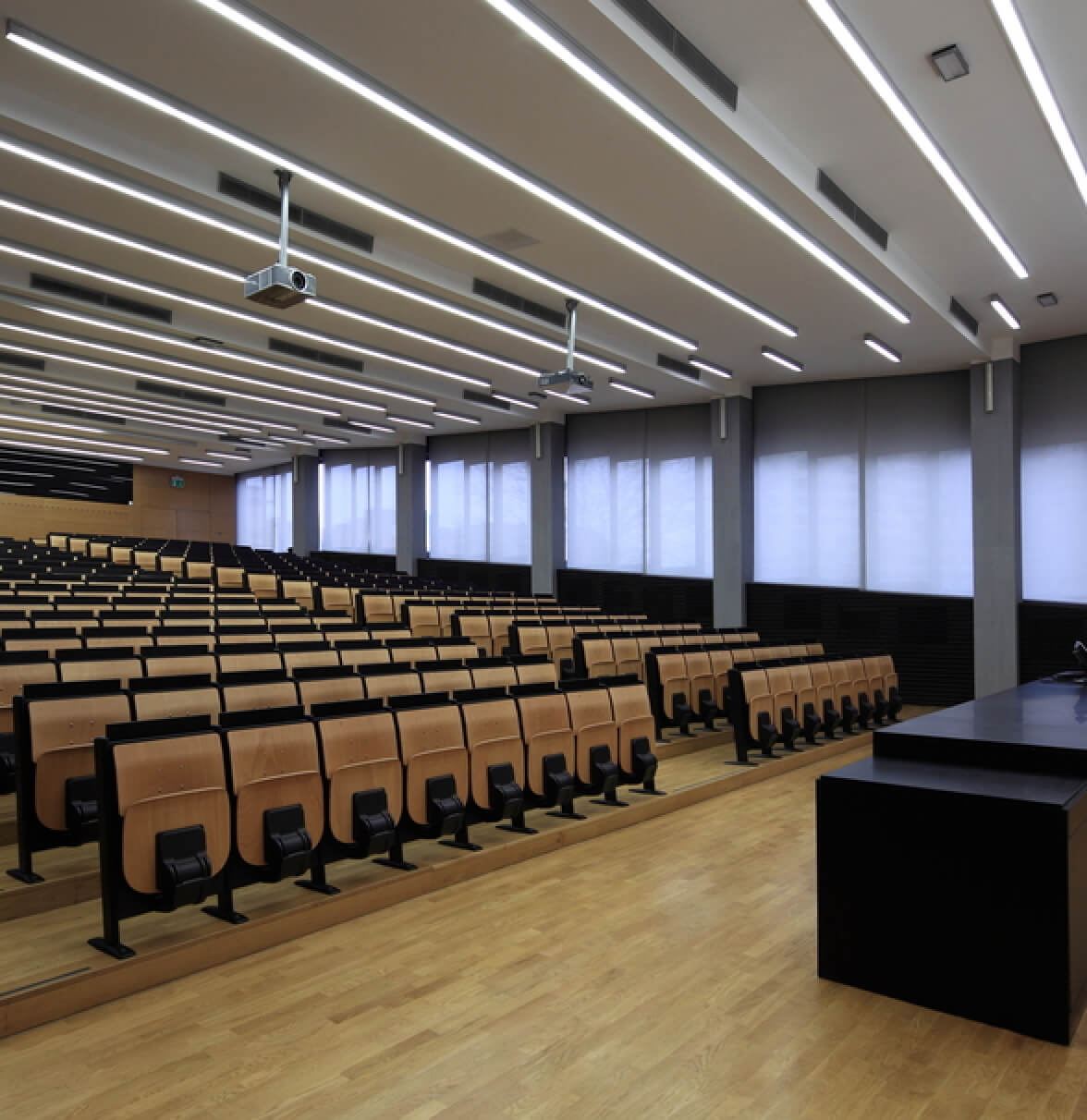 Modern lecture hall with wooden seating, large windows, and a sleek presentation area.