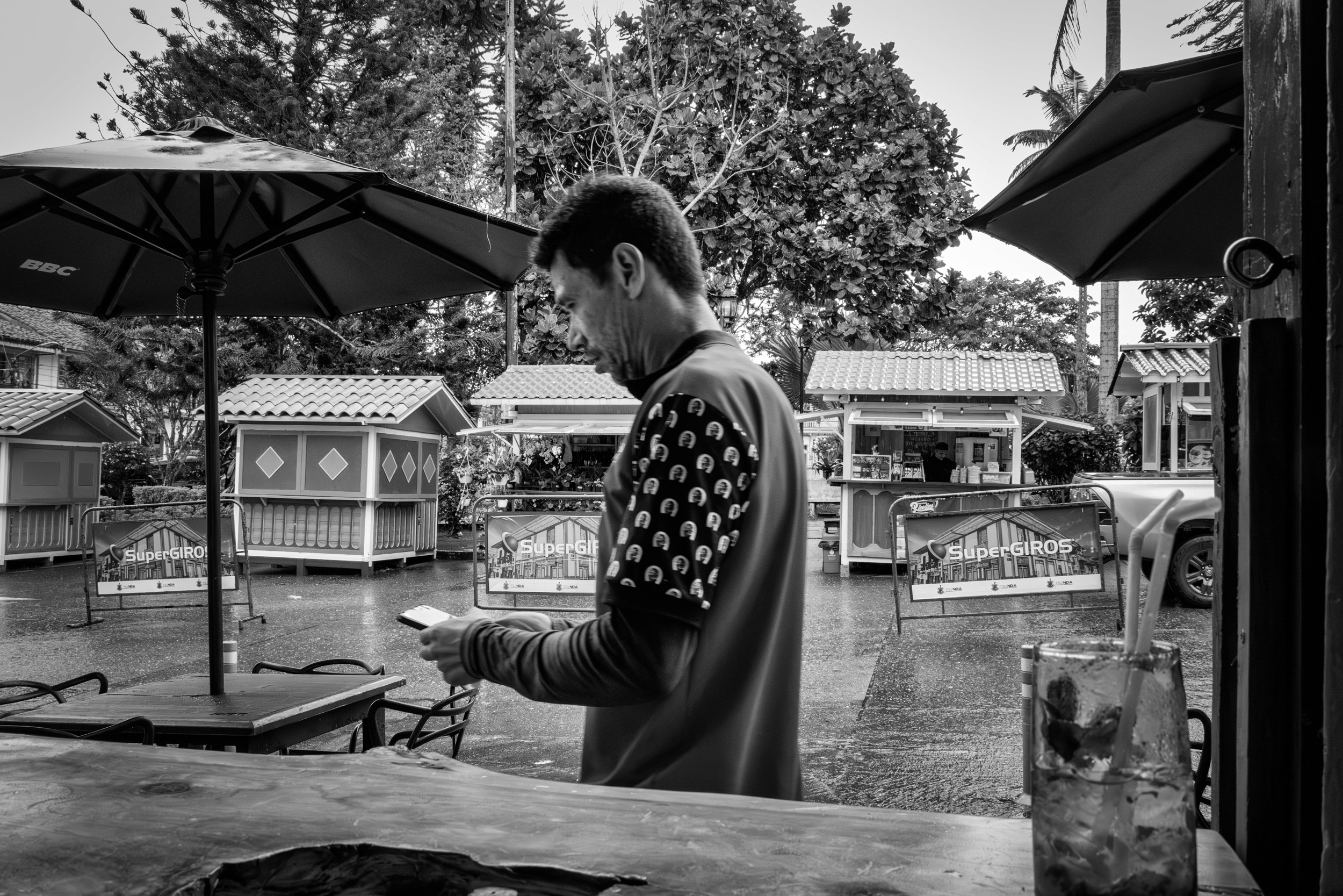 Rainy street scene with people passing by a bar window.