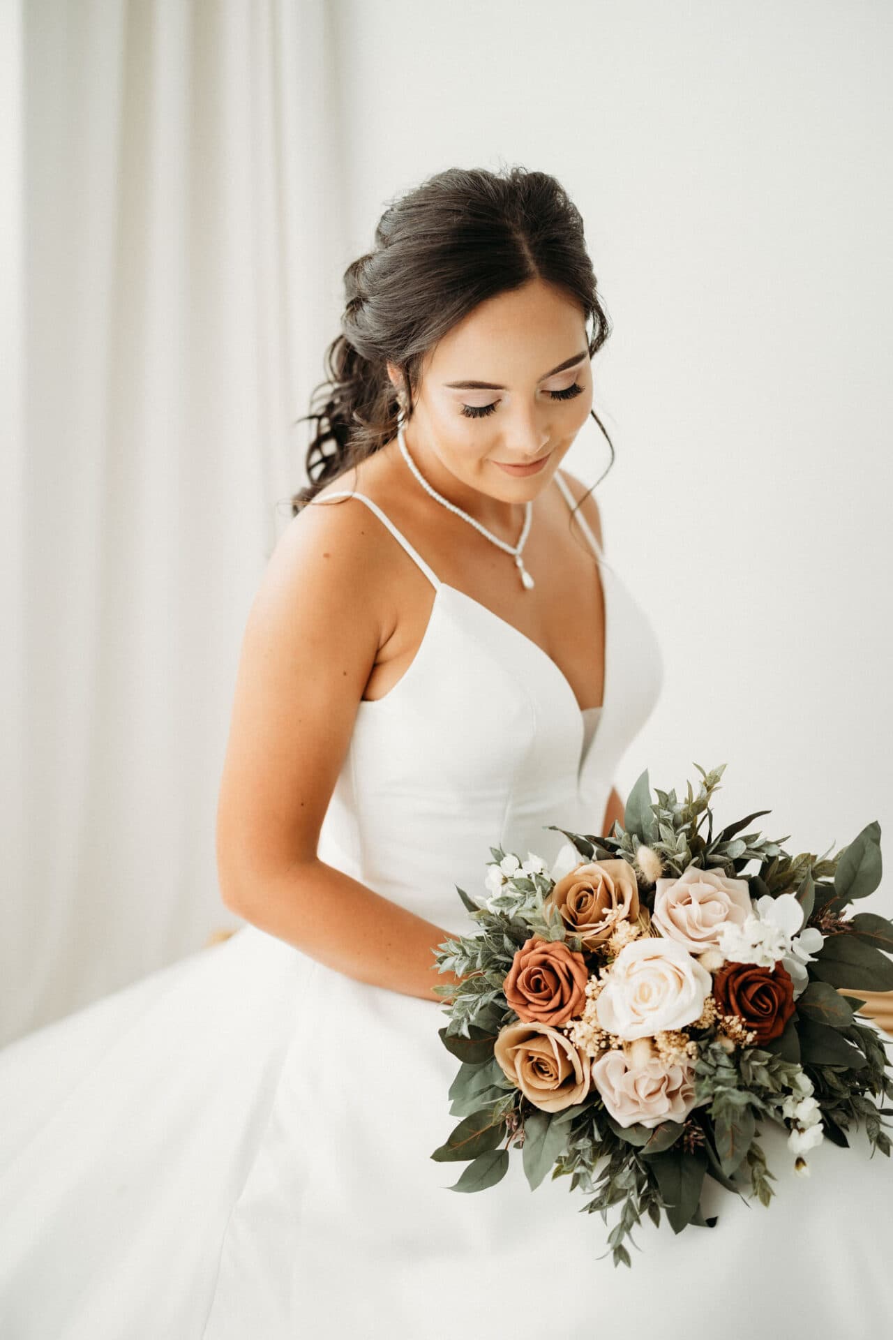 A bride holding a bouquet of flowers, looking down with a soft smile, photographed at Revelator Studio, a natural light studio in Shreveport, during a studio bridal session.