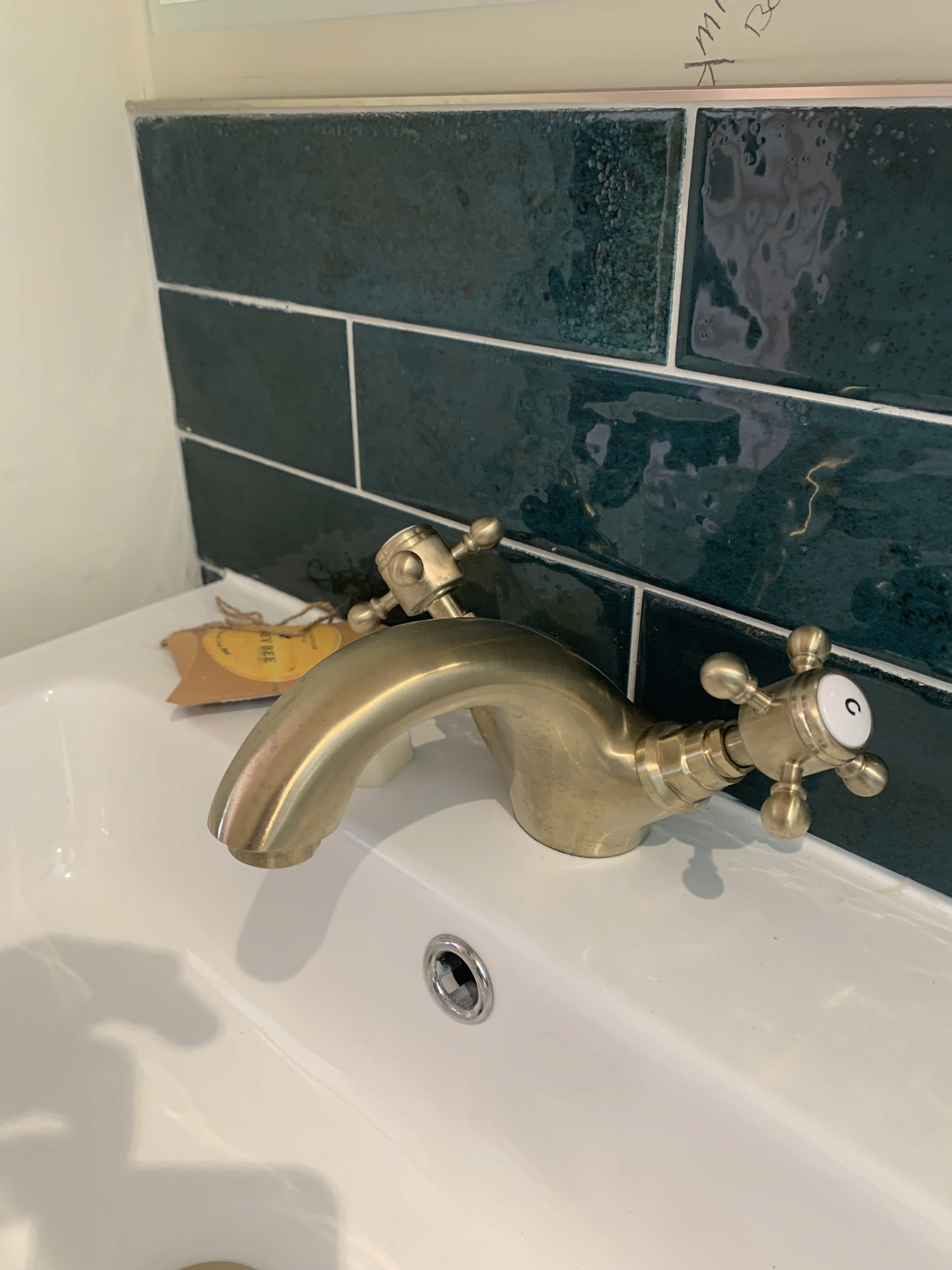 Brass basin taps over sink against green metro tiled wall