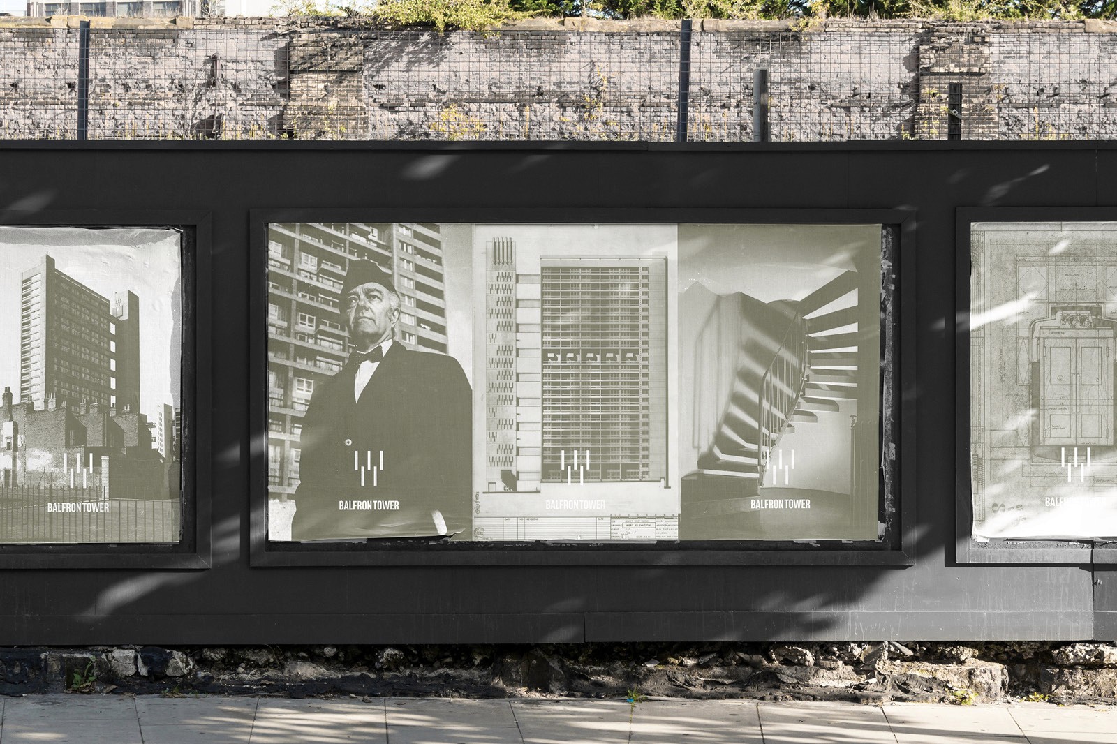 A modern street display showcases three black and white architectural posters for Balfron Tower, featuring tall buildings and a formally dressed figure, set against an urban backdrop with shadows cast by nearby trees.
