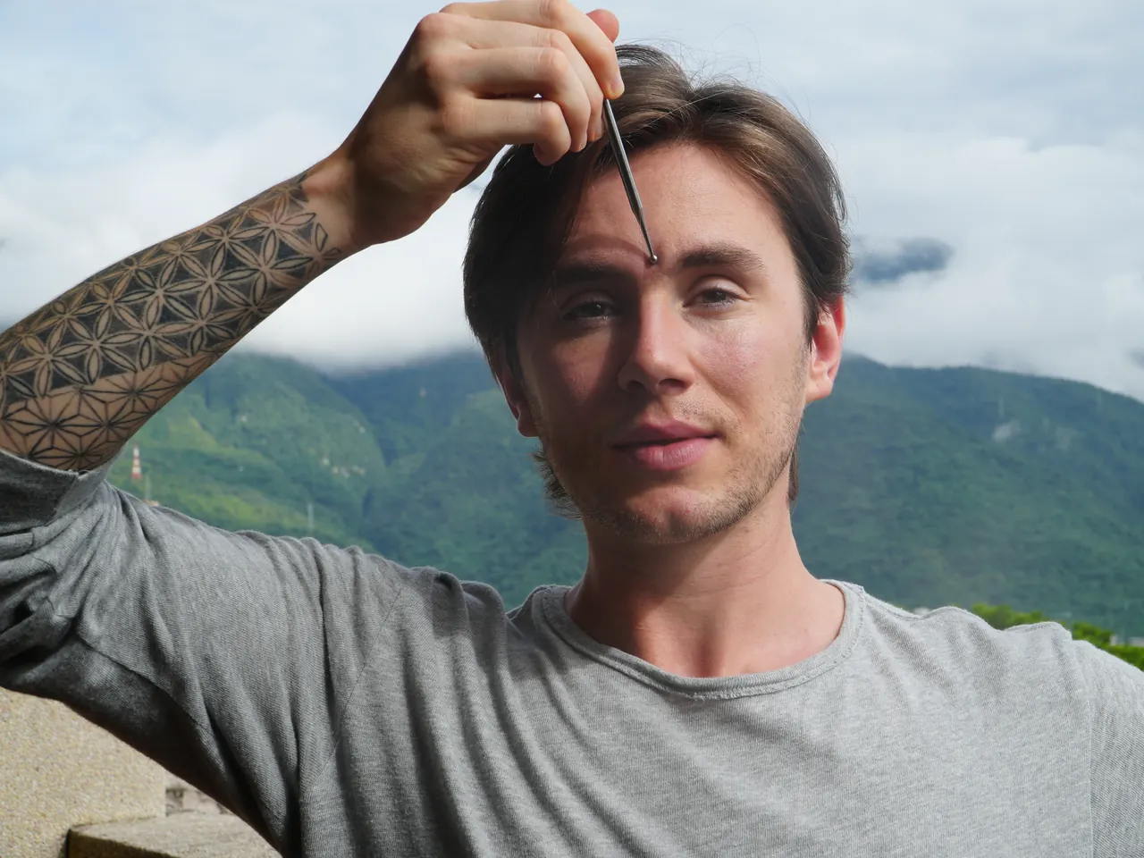 Jude Massey demonstrating facial acupressure with a slim steel tool, mountains behind him