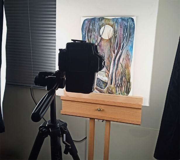 Camera photographing a painting on an easel.