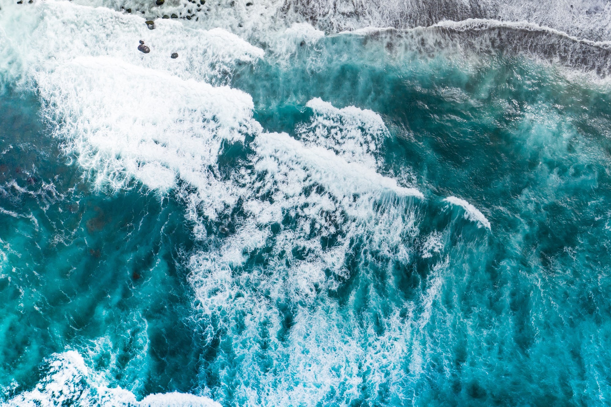 Aerial view of turquoise ocean water with white waves and foam creating a dynamic, vibrant seascape.