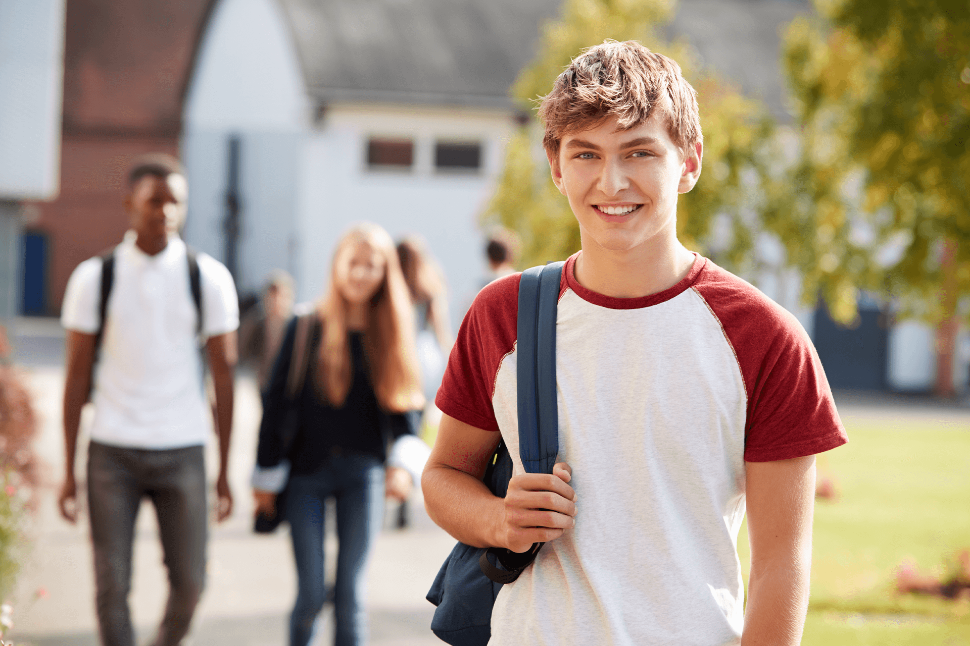 Happy boy leaving the learning centre smiling, with other students seen in the background walking and talking