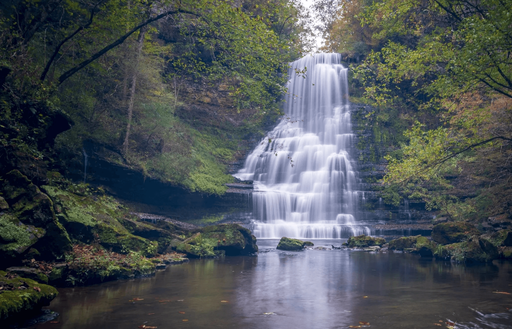 A rocky mountain landscape with a cascading waterfall flowing down its cliffs surrounded by greenery.