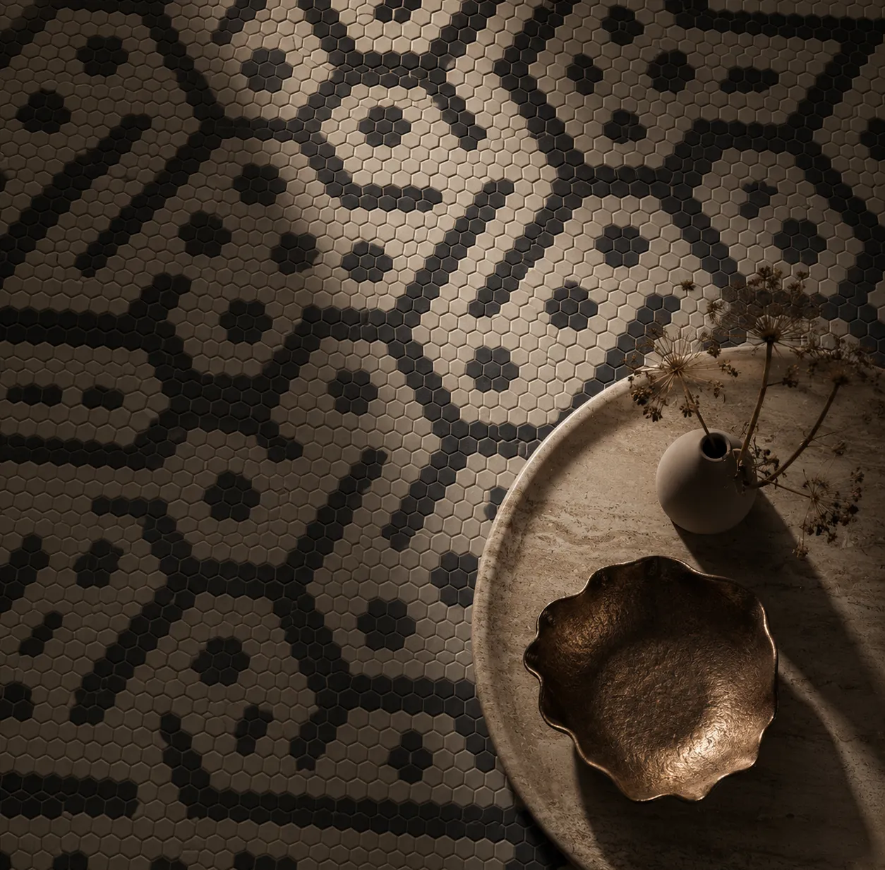Flowin modular marble mosaic floor in beige and dark natural stone, photographed with a circular stone table in a moody interior.