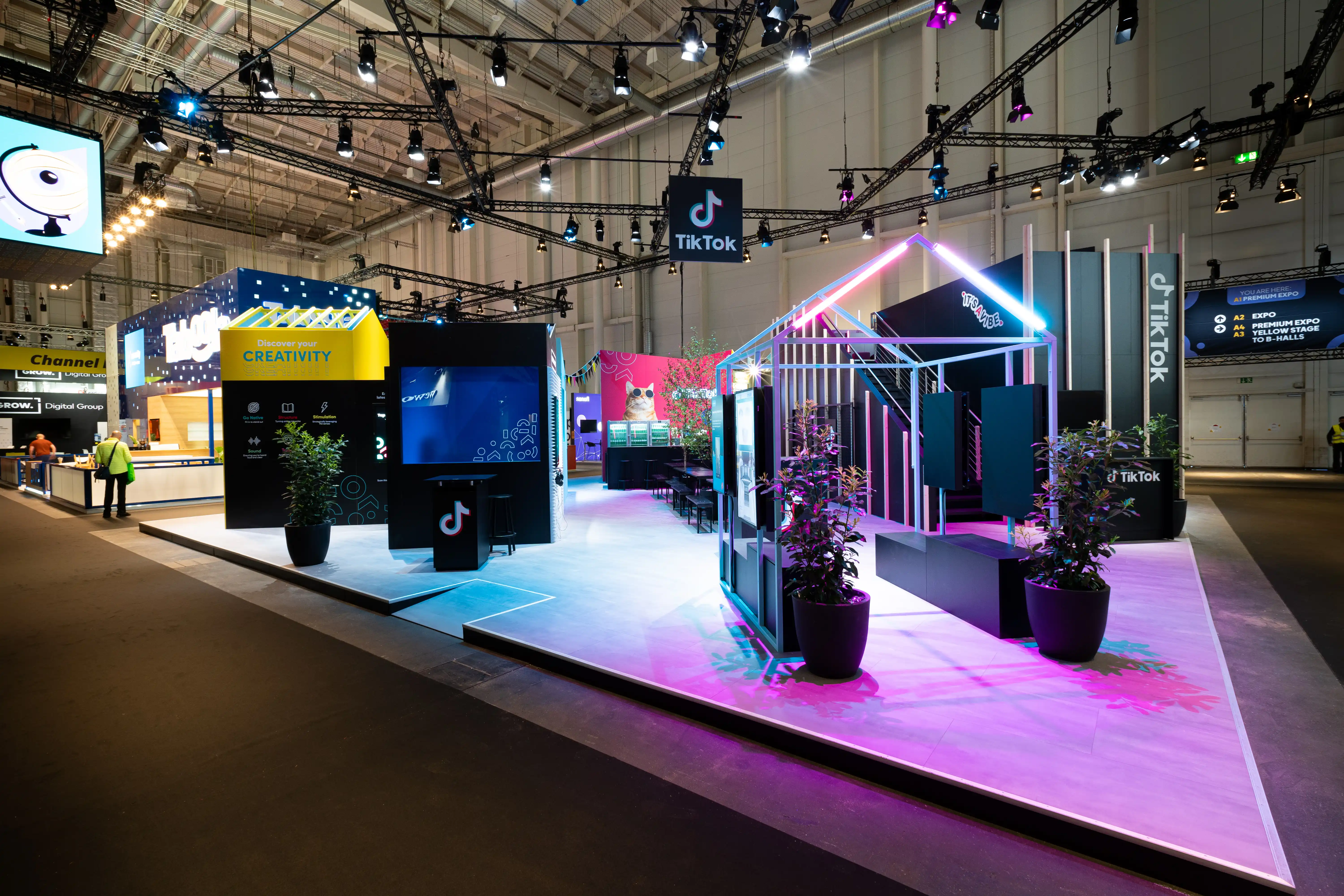 Overview of the colorful TikTok village at OMR with yellow Creativity house, screens, plants and glowing house frame.