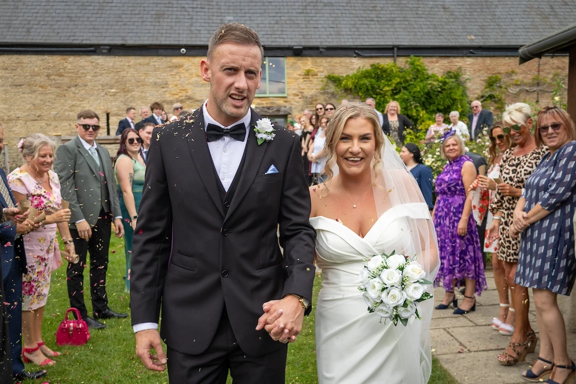 Charlotte and Chris walking through confetti after their ceremony at The Great Barn Aynho