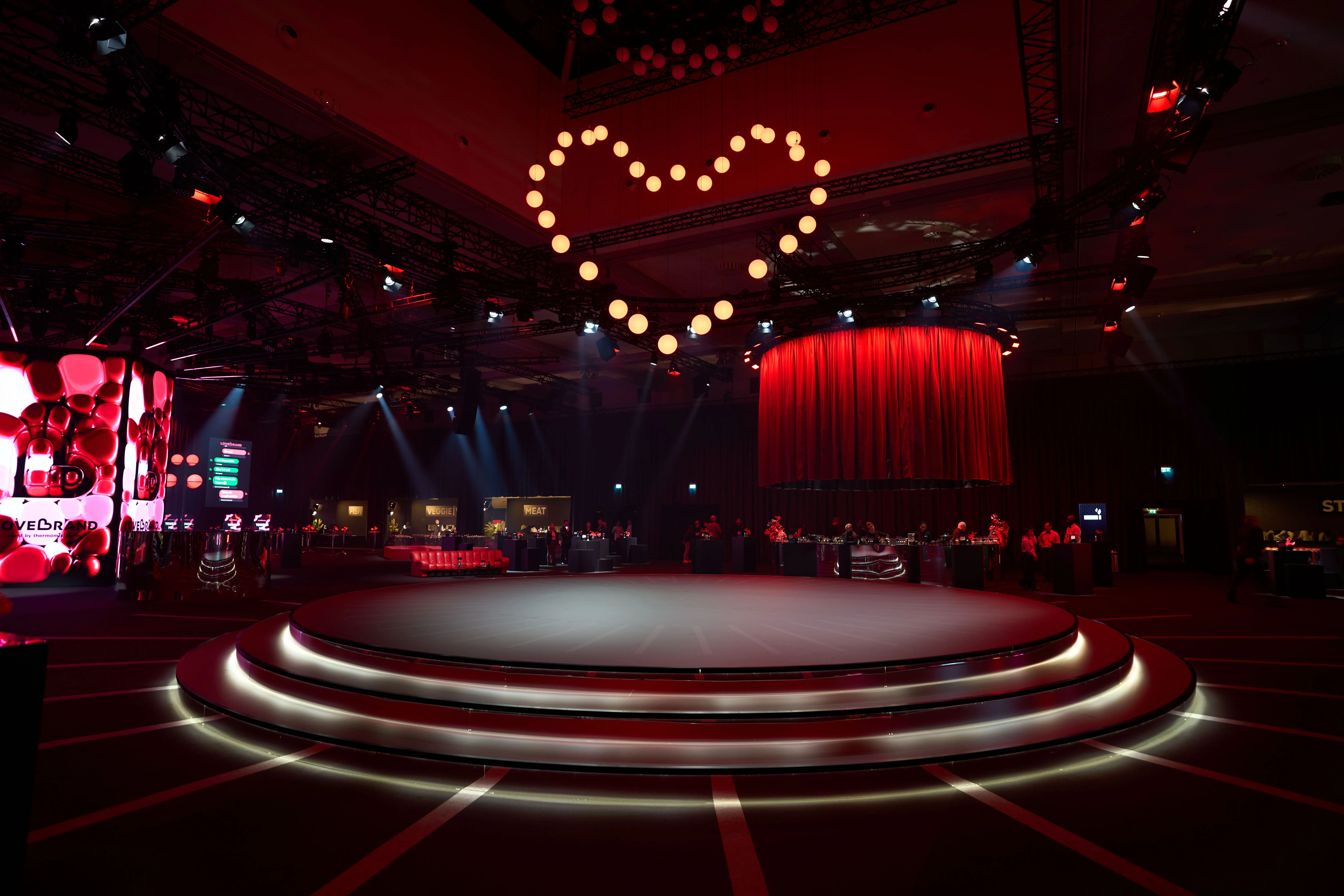 Round stage under a heart of glowing spheres with red curtain in the dark hall.