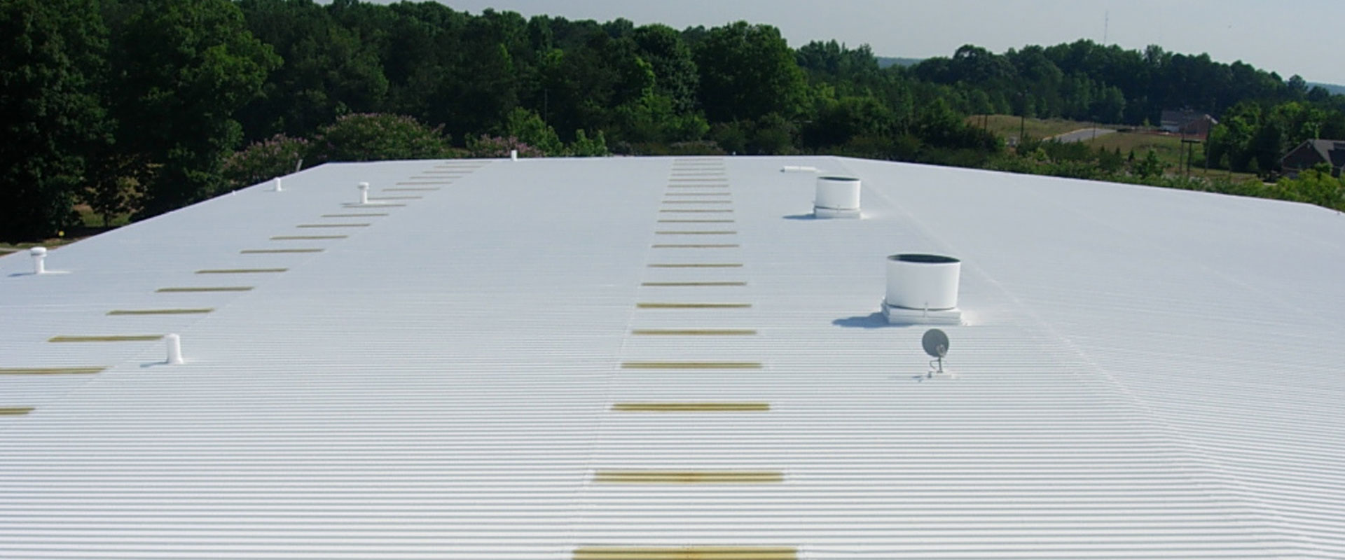 Large commercial building with a bright white acrylic roof coating, reflecting sunlight to improve energy efficiency and protect against weather damage.