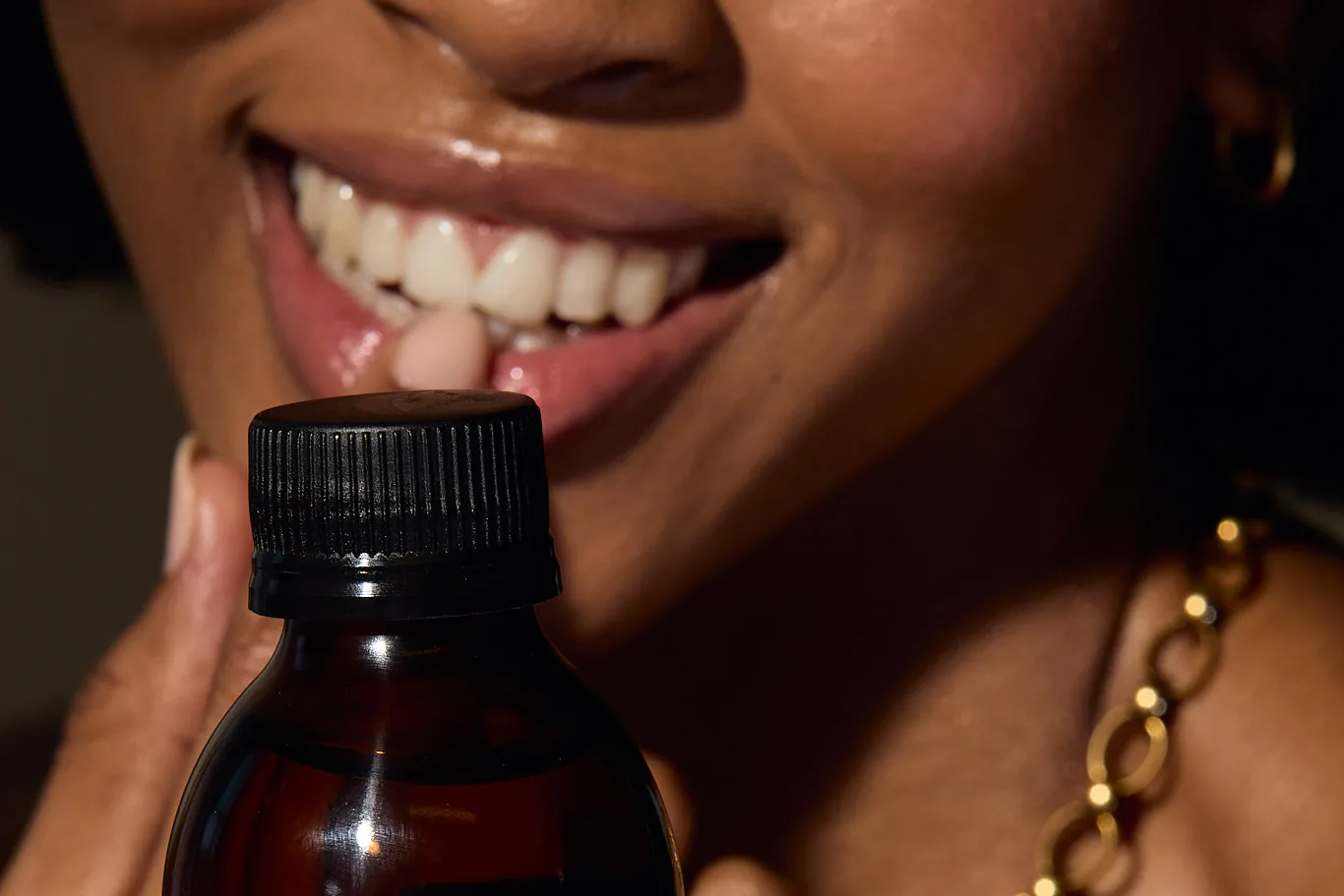 A smiling woman holds a bottle of Sēkret Queen syrup in golden light