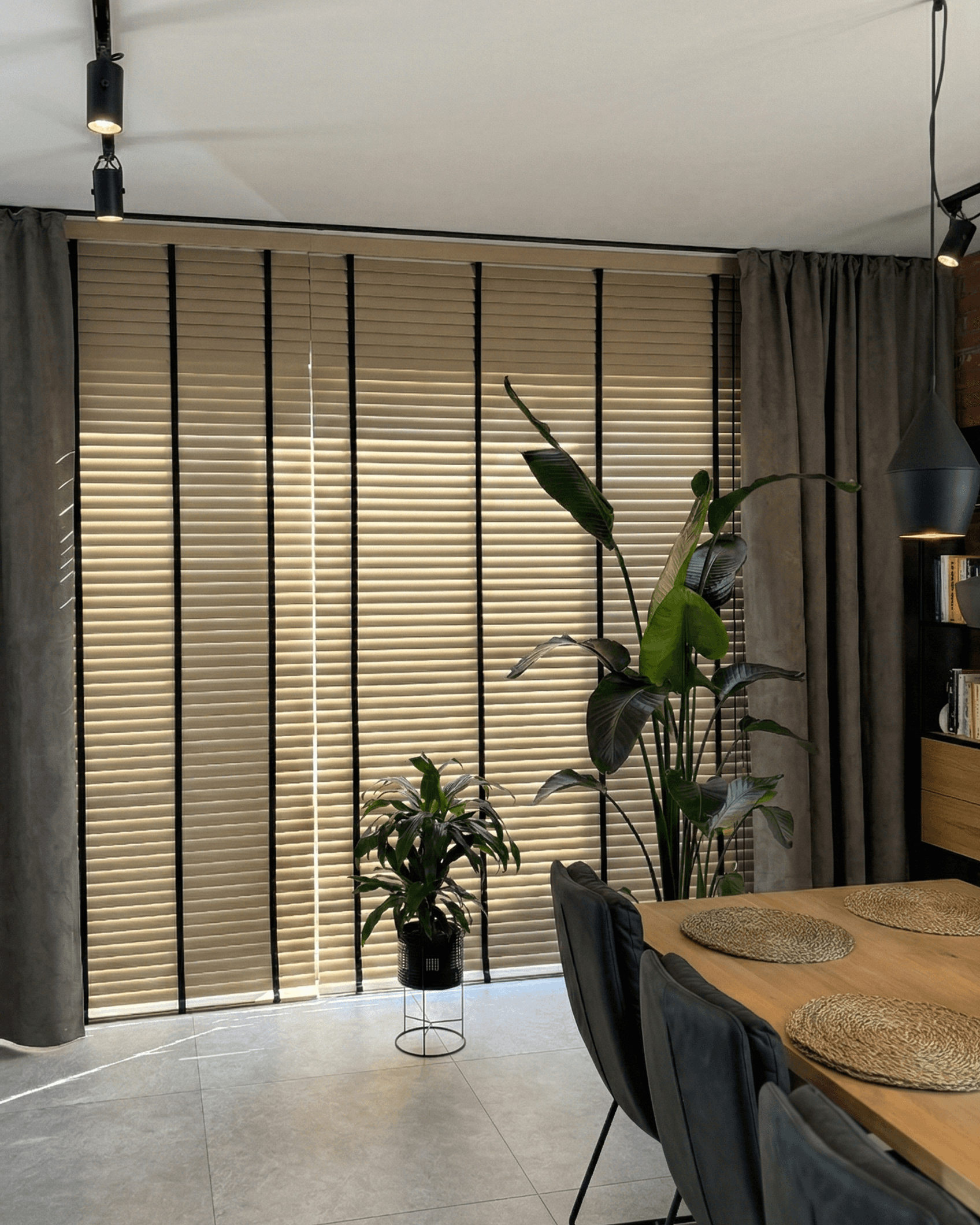 Szerokie żaluzje drewniane z dekoracyjnymi czarnymi taśmami w nowoczesnej jadalni. Profesjonalne osłony okienne na wymiar HeyShade Pruszków – elegancja i prywatność.