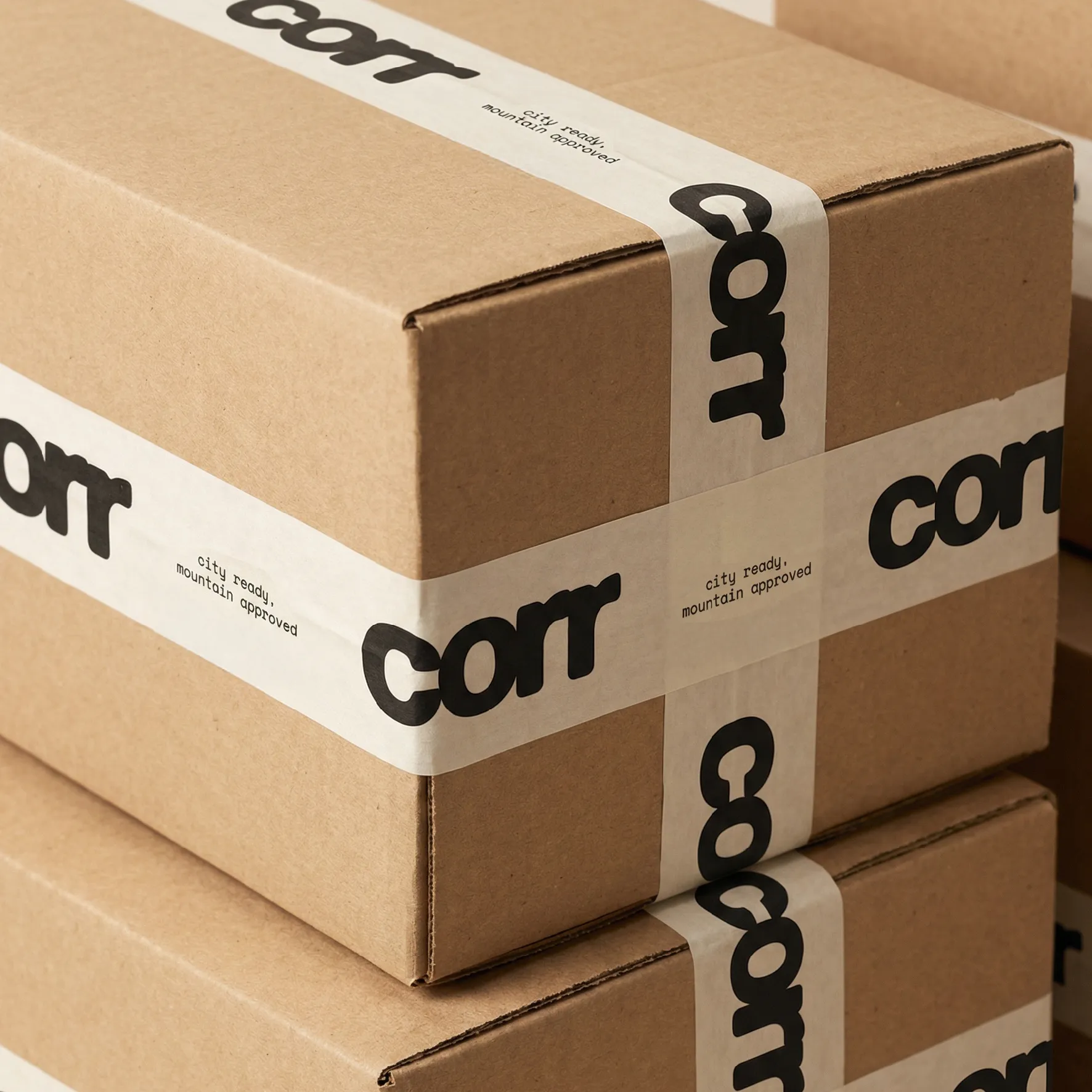 A brown packaging box with white tape and branded elements involving their wordmark and slogan printed on the tape. The boxes stacked ontop of each other.