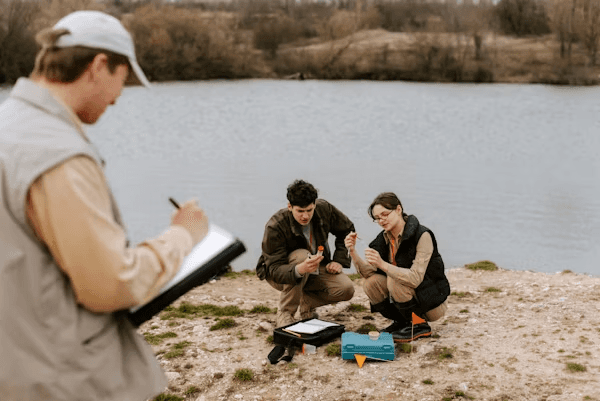 High school student conducting environmental science research with a PhD mentor, analyzing ecological data on a laptop outdoors