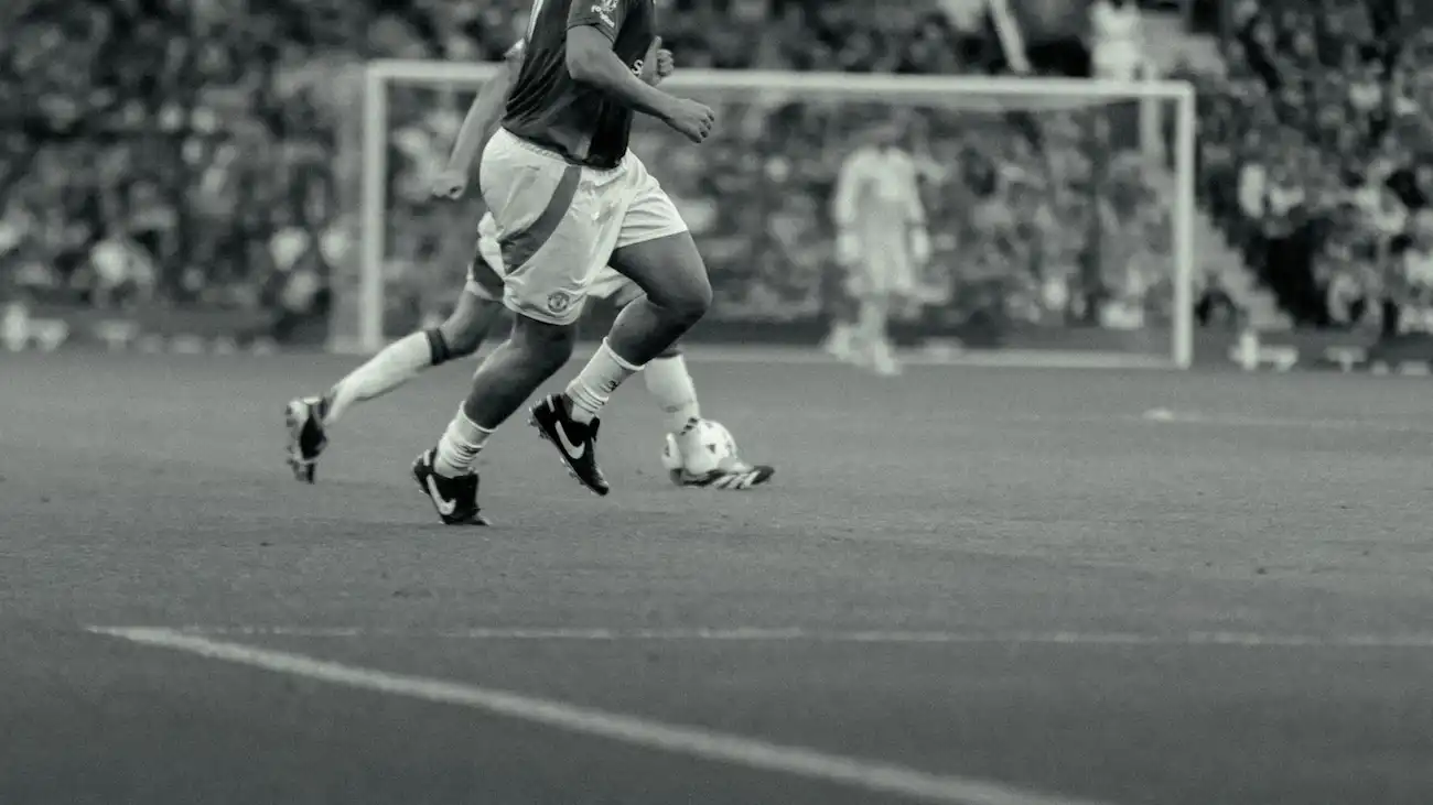 Black-and-white photo of a football player dribbling the ball during a match — illustrating the history of sports sponsorship from early kit branding to today’s digital-era activations.