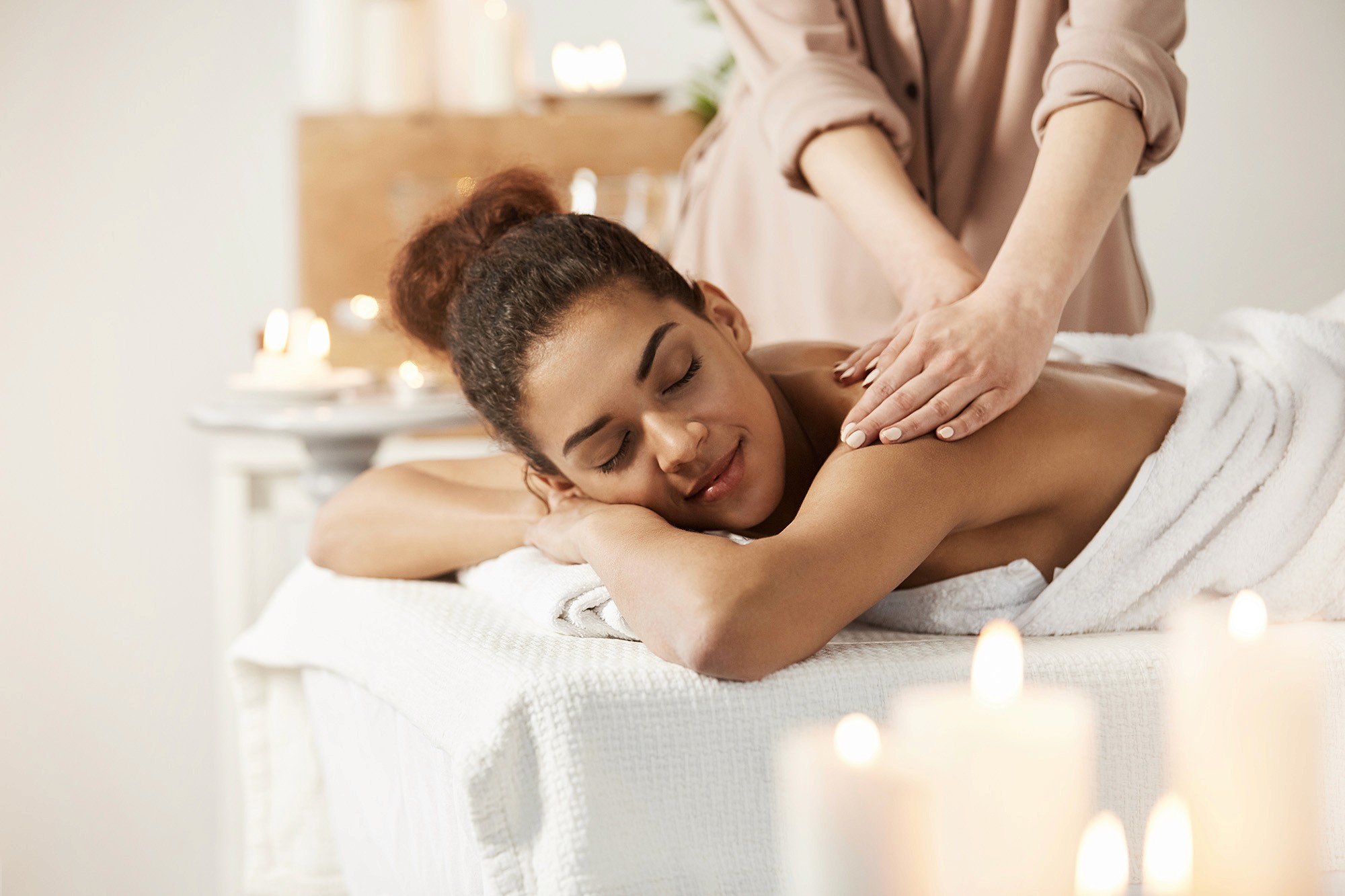 Woman relaxing on a massage table with candles in the background, receiving a back massage in a spa setting