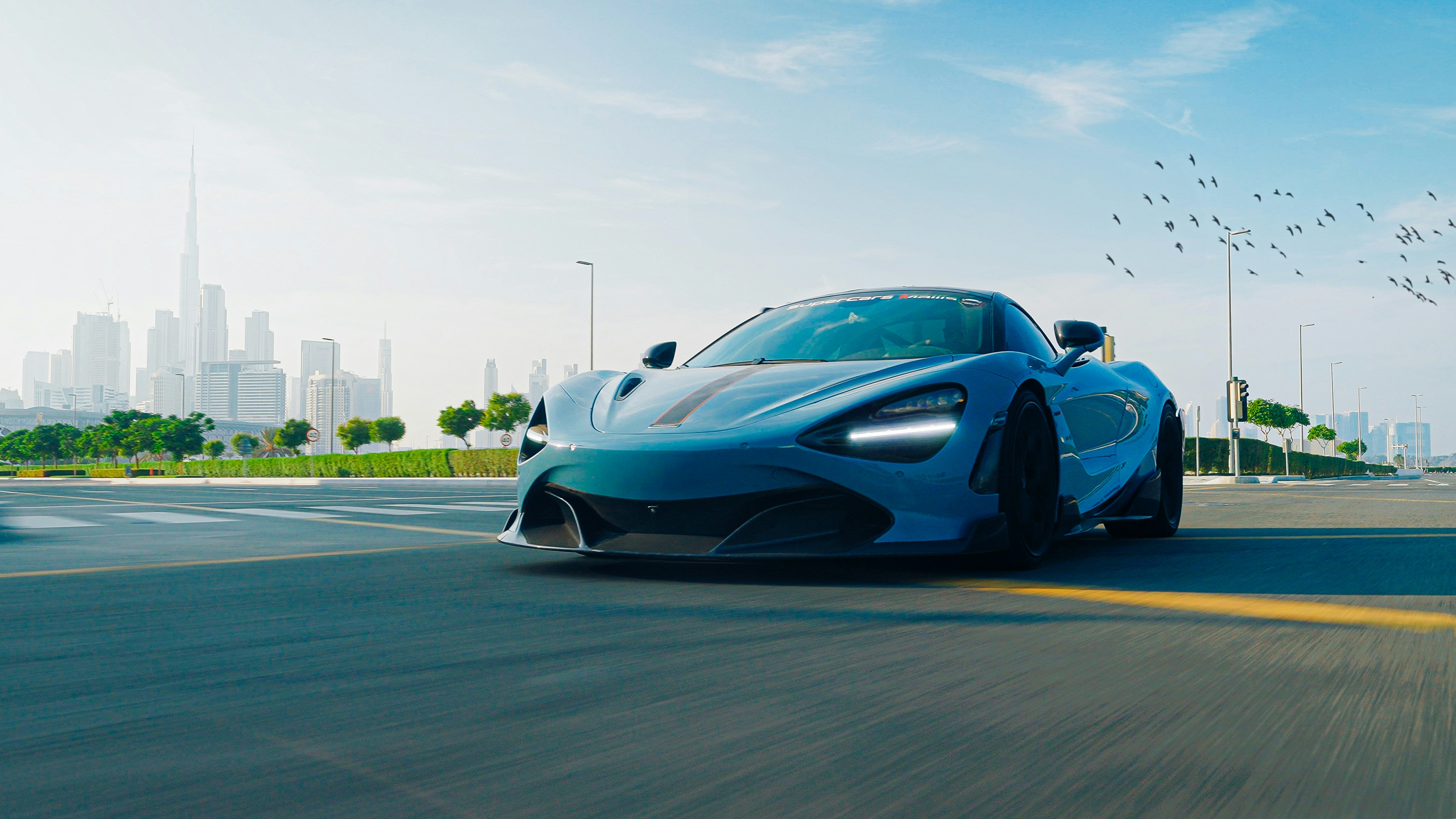 A sleek, high-performance sports car speeds down an urban highway with a modern city skyline in the background, set under a clear blue sky, emphasizing luxury and speed.