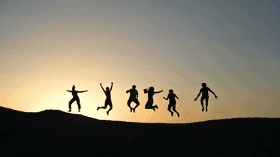 Silhouettes of friends jumping together on a hill at sunset, illustrating the liking principle
