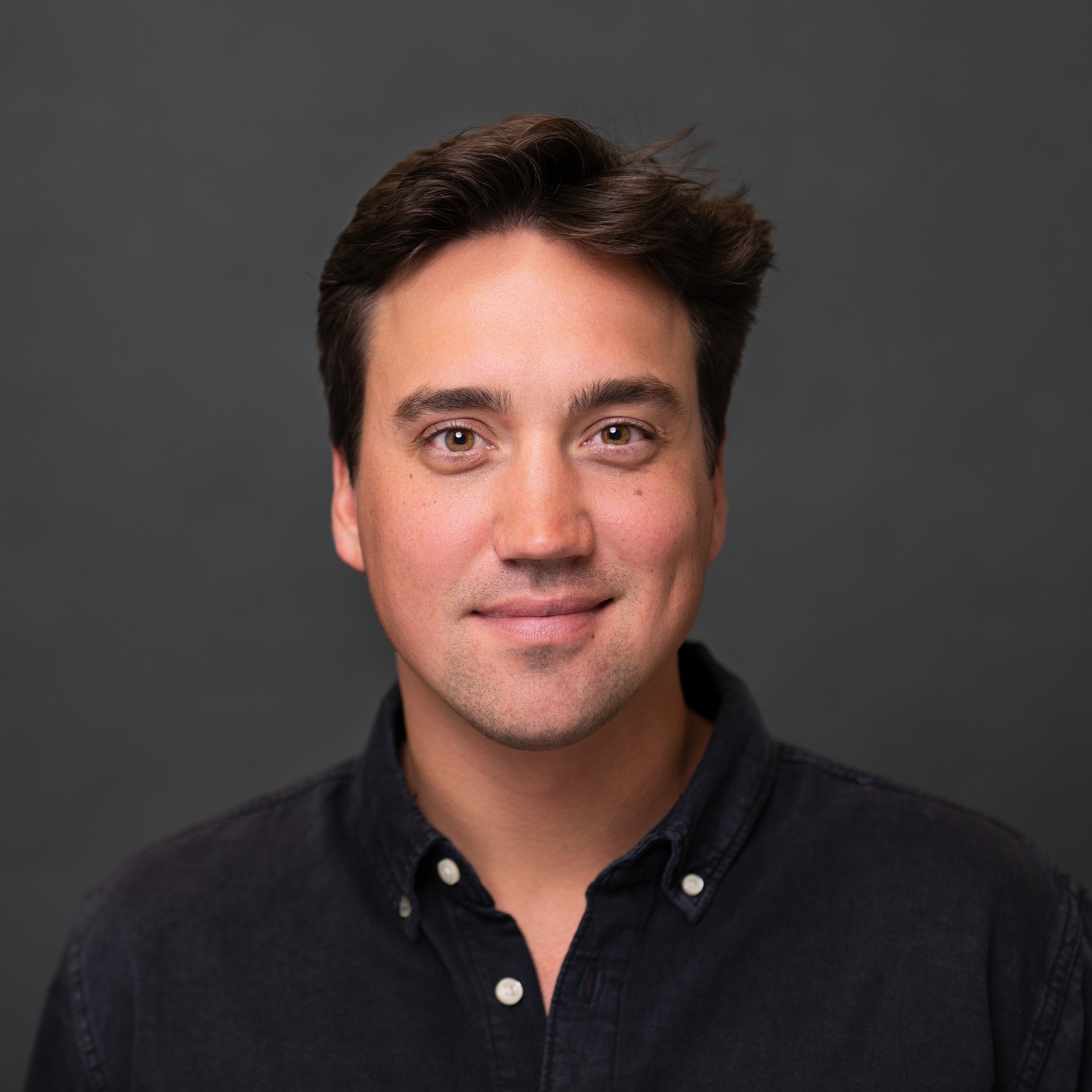 Man in a black shirt photographed for a headshot against a dark gray background