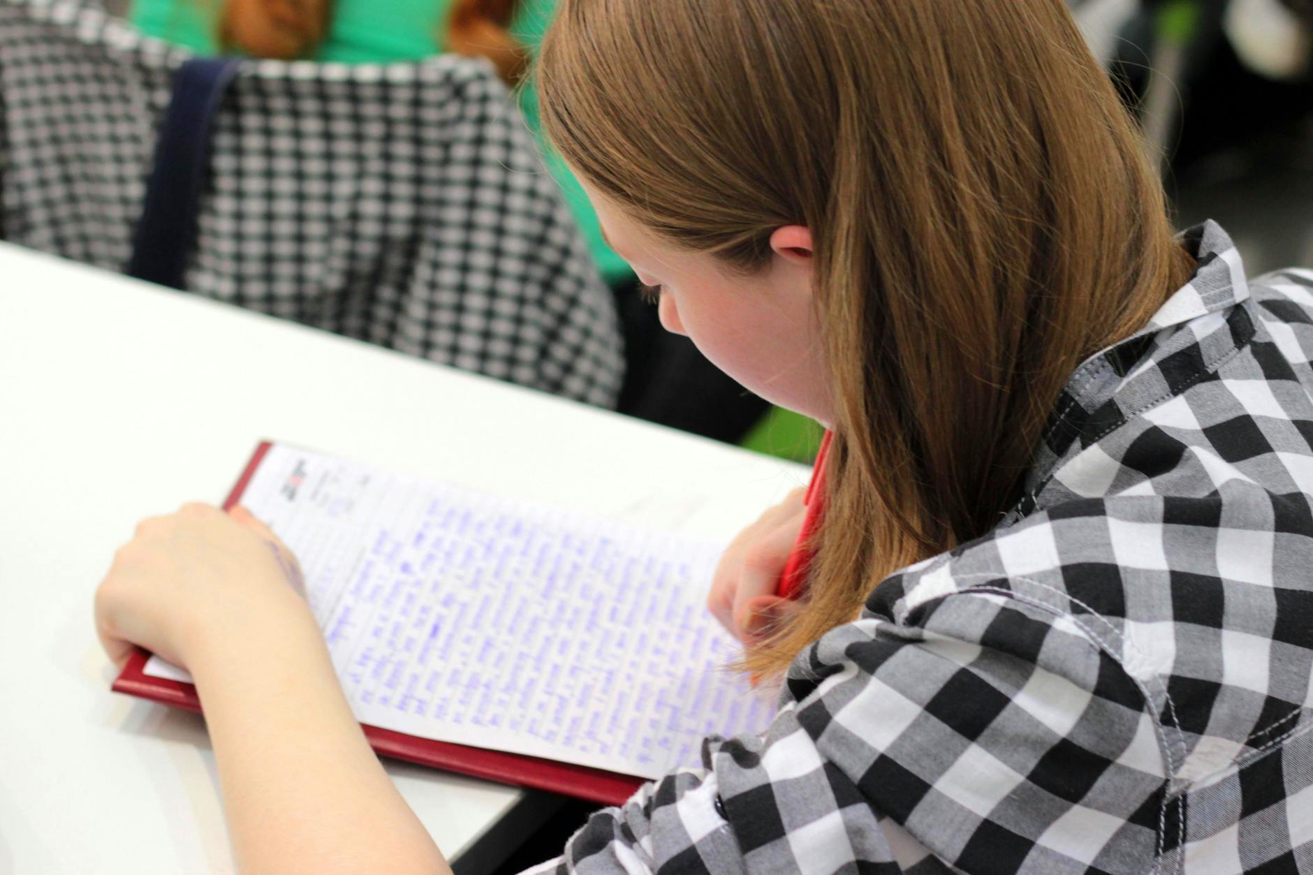Close-up of a teachers hands using a red pen to write constructive feedback on a student's open notebook.