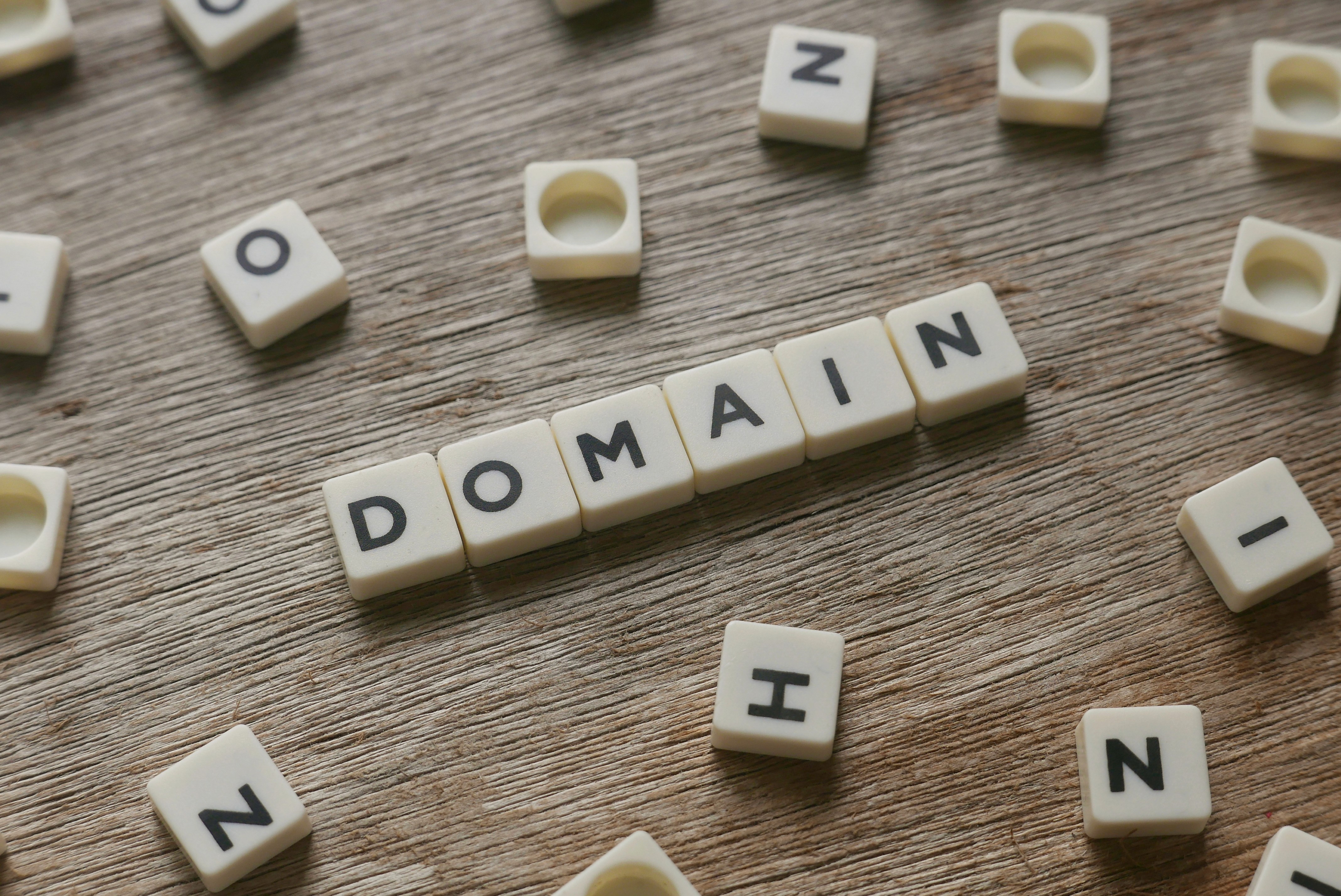 Scrabble-style letter tiles spelling the word 'DOMAIN' on a wooden surface, representing domain name registration and website setup