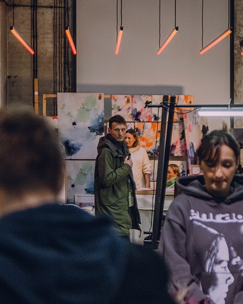 Zdjęcie przedstawiające kilka osób na targach, którzy oglądają obrazy i sztukę.