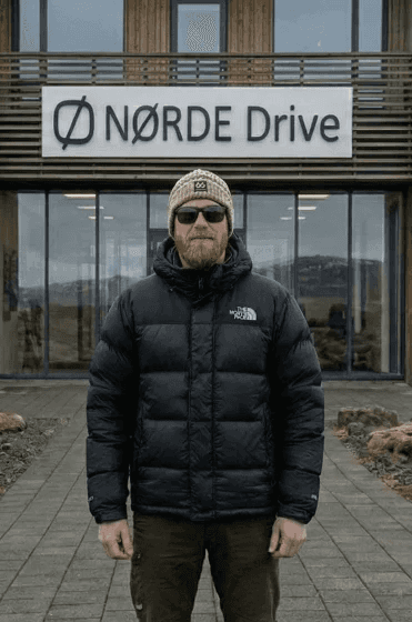 Man in a black puffer jacket standing outside a building with glass windows.