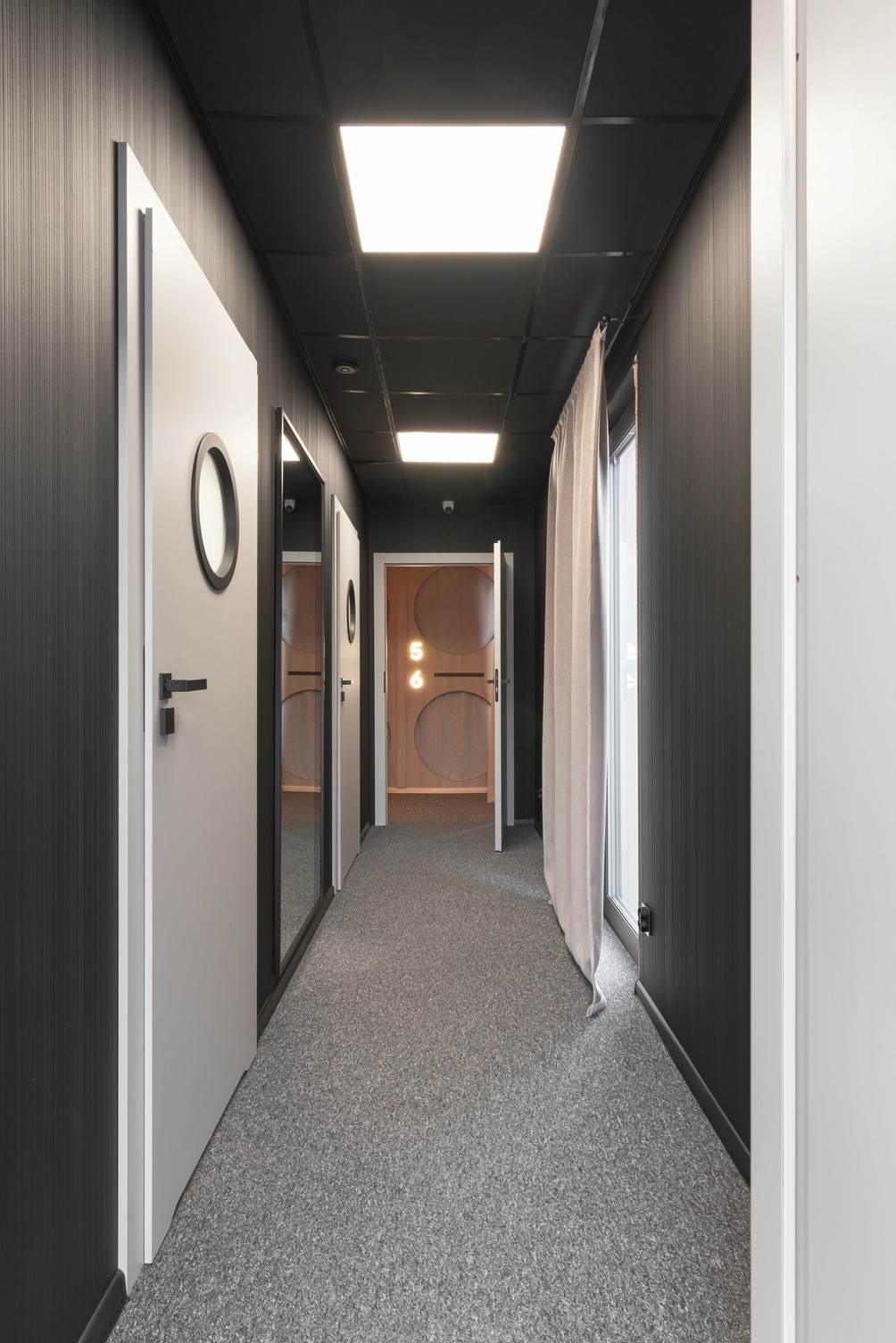 Modern hallway with wood paneling, recessed lighting, and a mirror wall. Soft lighting and neutral tones create a warm atmosphere.