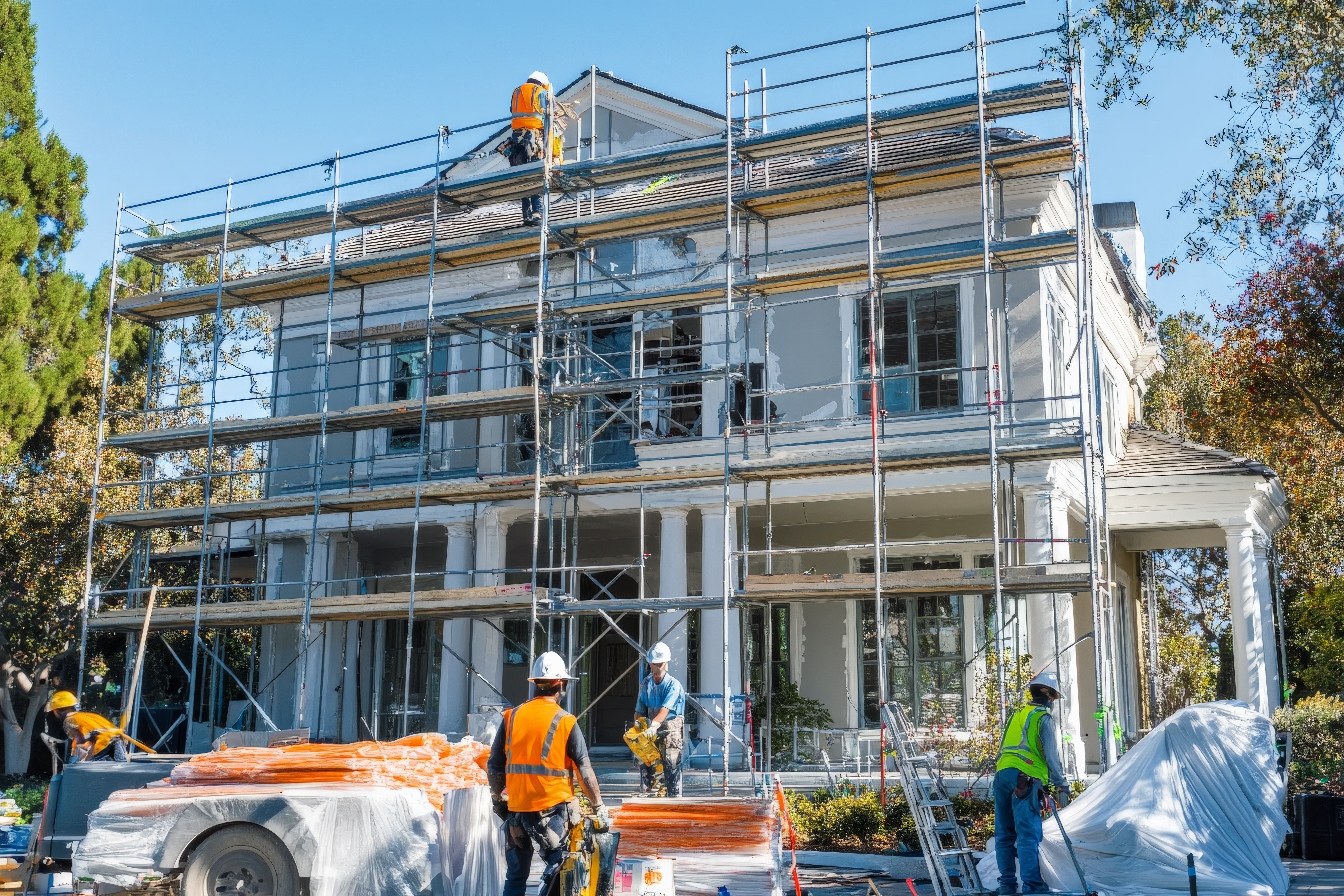 Home restoration in progress on a two-story house in St. Louis with scaffolding, construction workers, and roofing materials under clear blue skies.