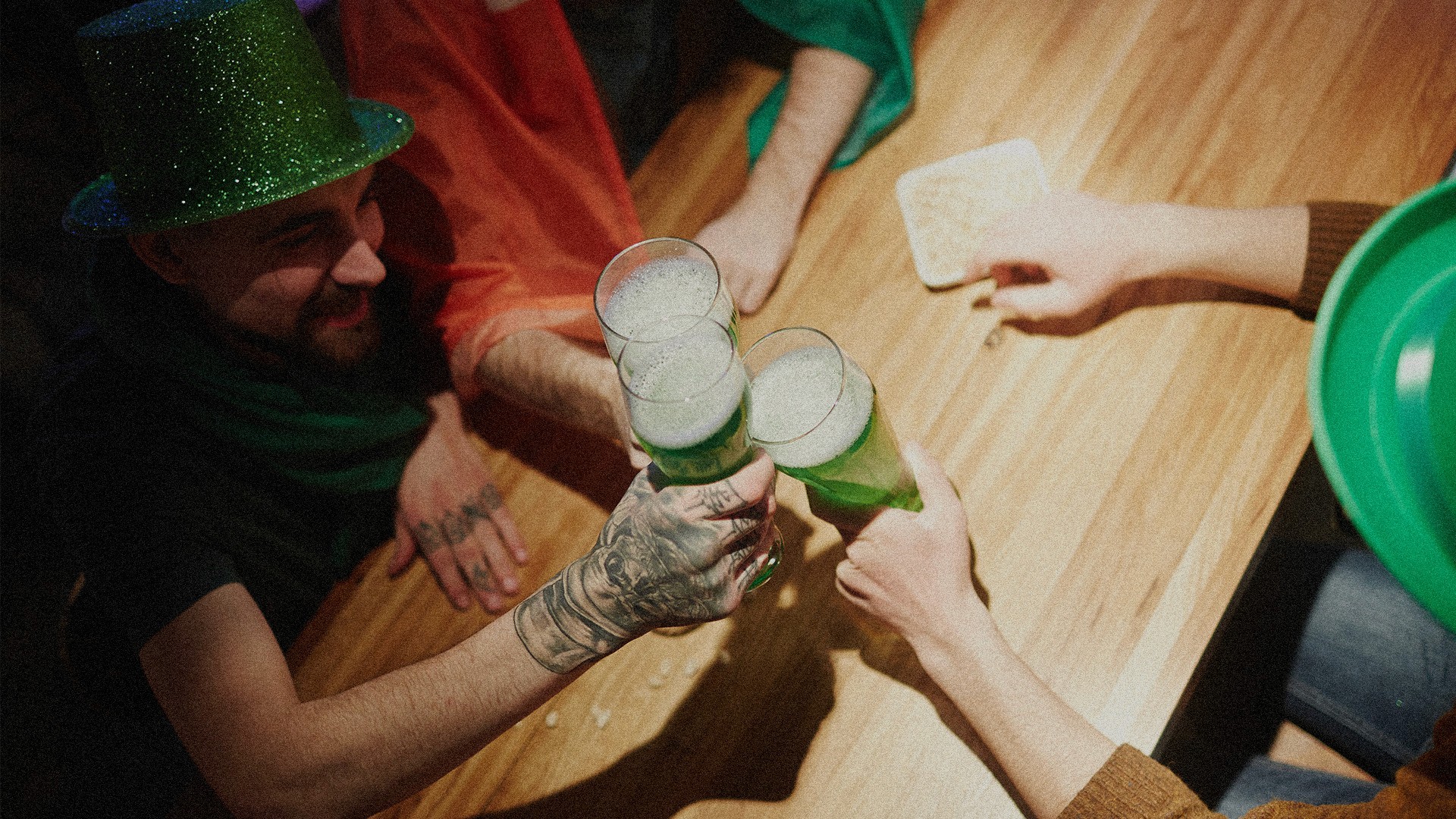 A group of people celebrating St. Patrick's Day at a bar doing cheers with their beer that is green.