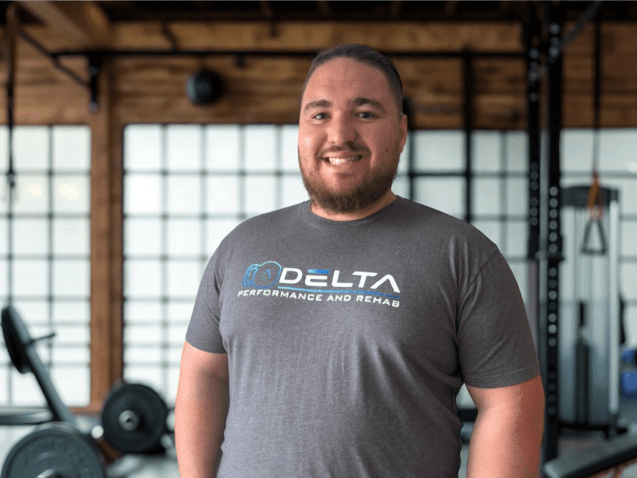 Smiling team member wearing a Delta Performance and Rehab shirt inside a strength training facility—representing expert care, trust, and athlete-focused therapy.