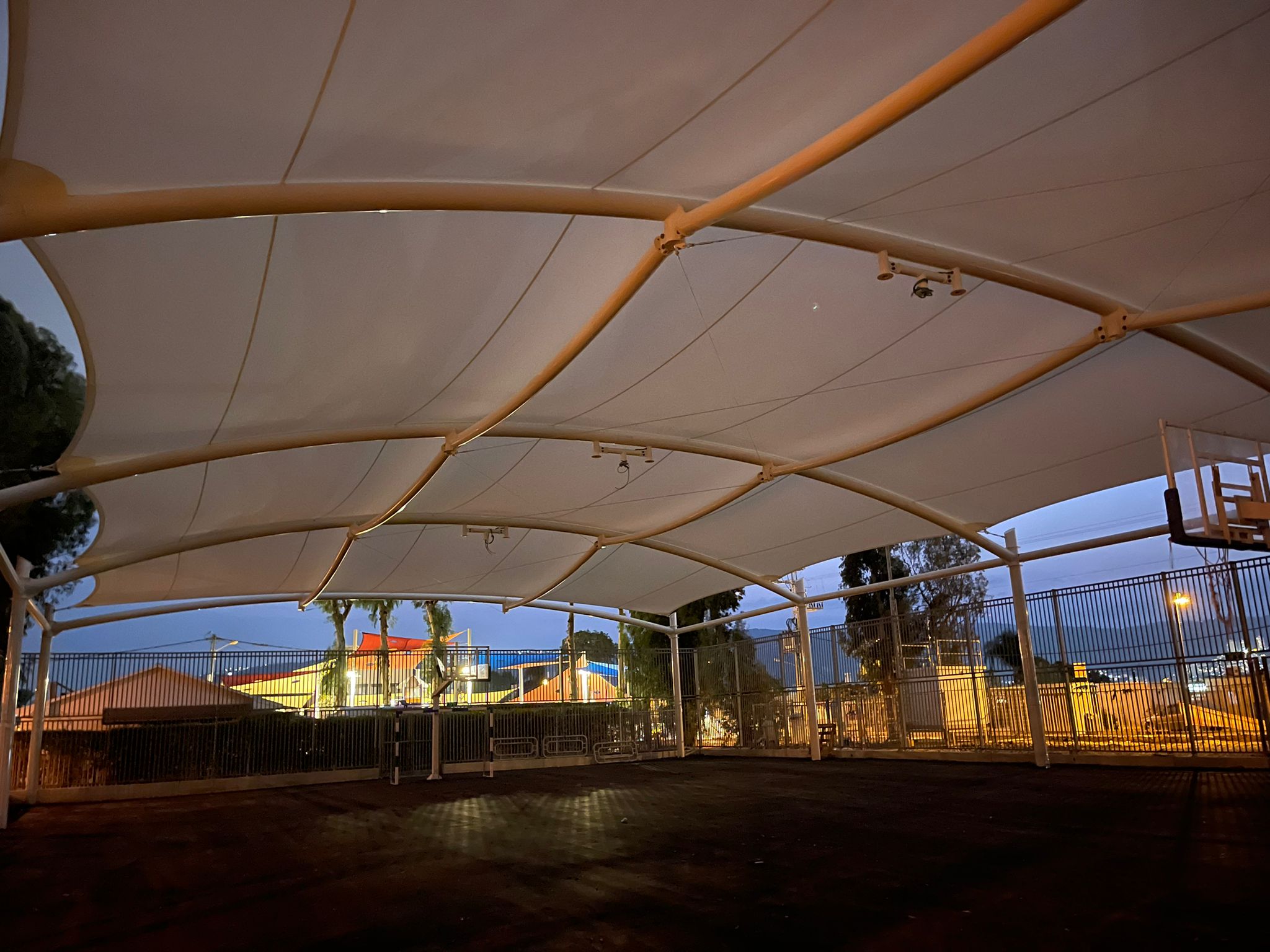 Covered outdoor area with beige fabric roof and metal frame at dusk.