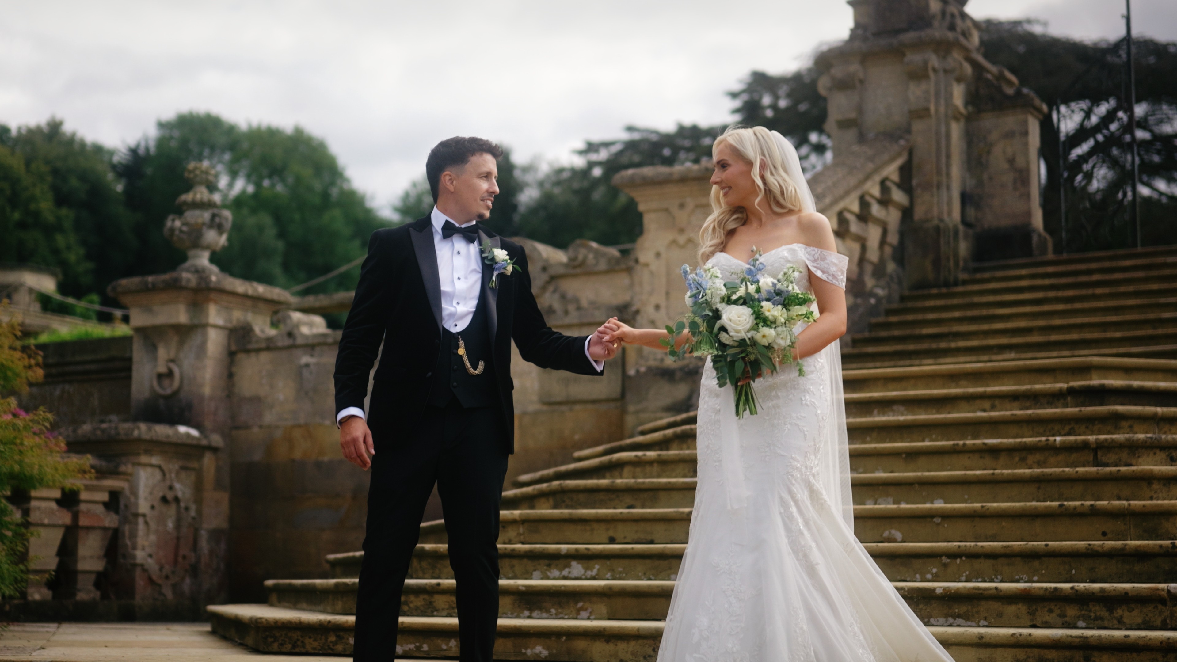 Bride and groom holding hands during wedding portraits on the stone steps at Harlaxton Manor in Lincolnshire