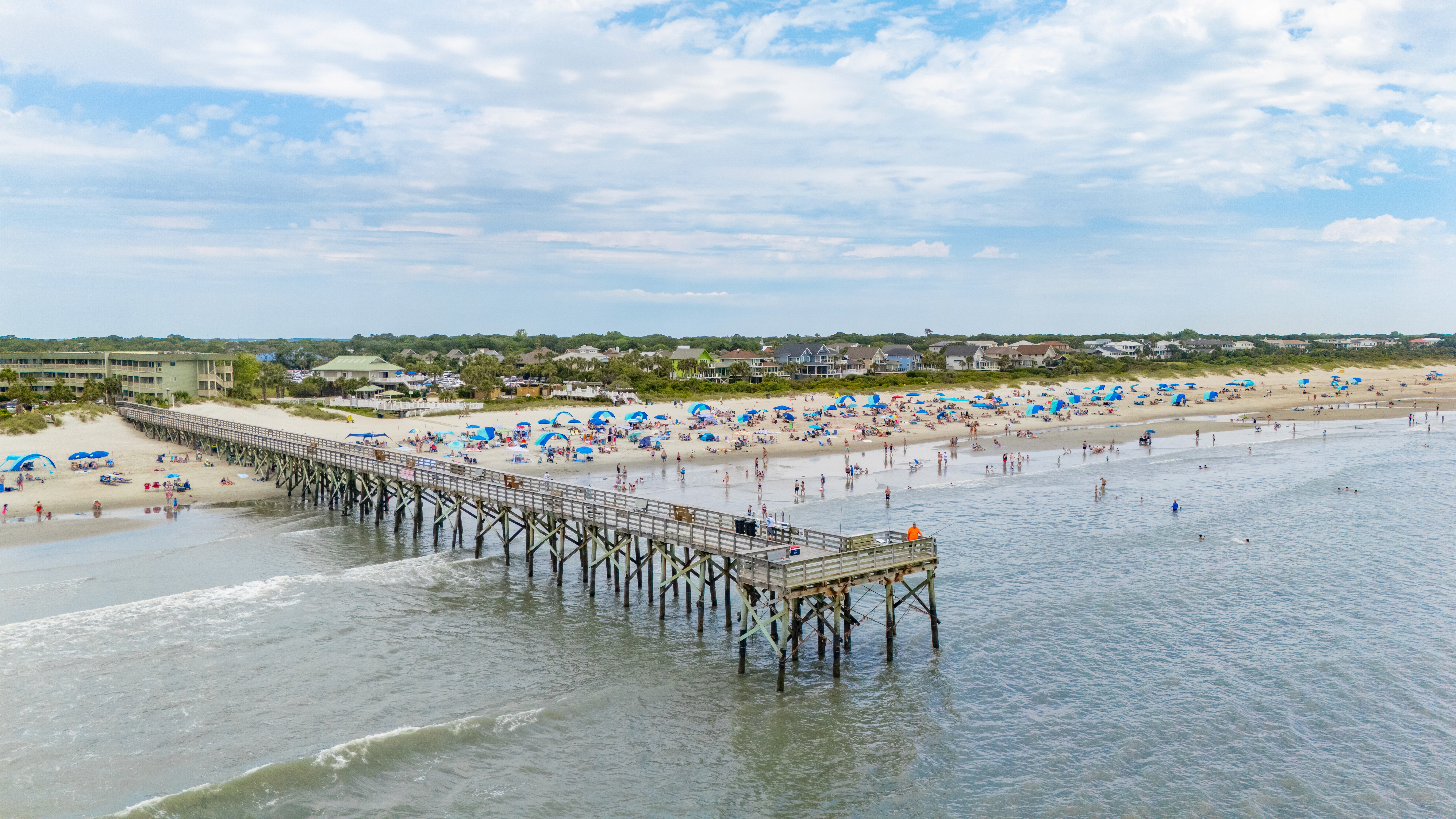 Crowds enjoying a sunny holiday weekend on Isle of Palms Beach, with the pier in view and colorful umbrellas dotting the sand.