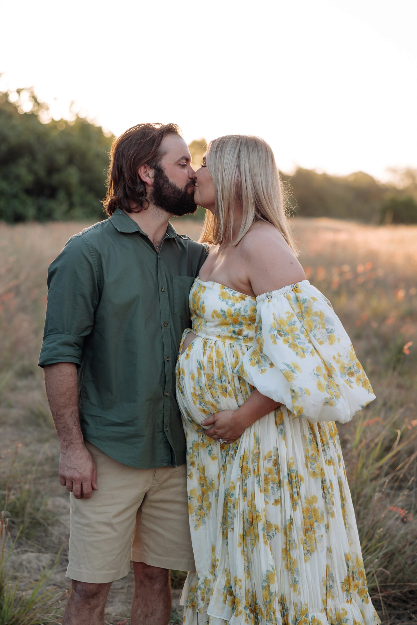 Mackay maternity photographer documenting pregnant mother and father embracing in tall grass at sunset