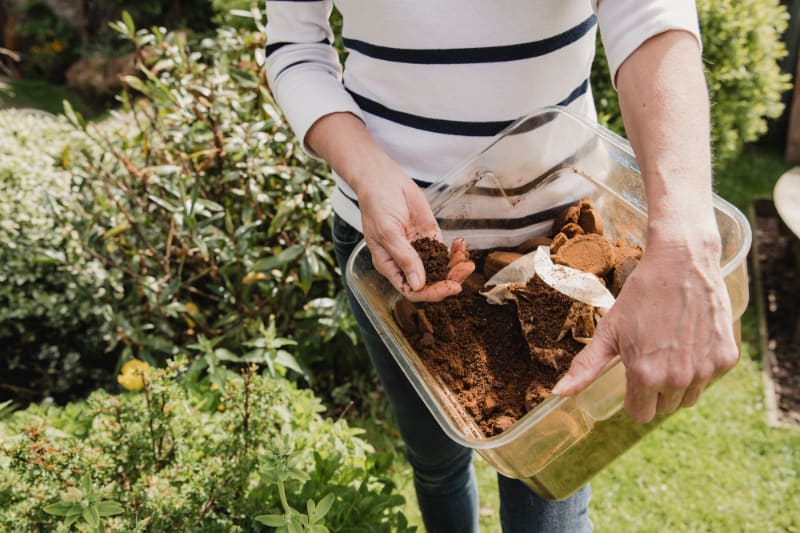 woman holding container with coffee grounds outside