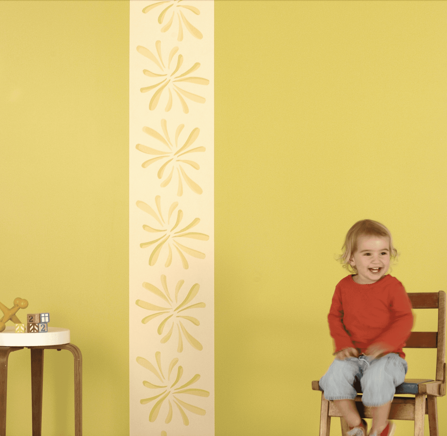 Child sitting on a chair in front of a vertical band of wallpaper installed on the wall behind them.