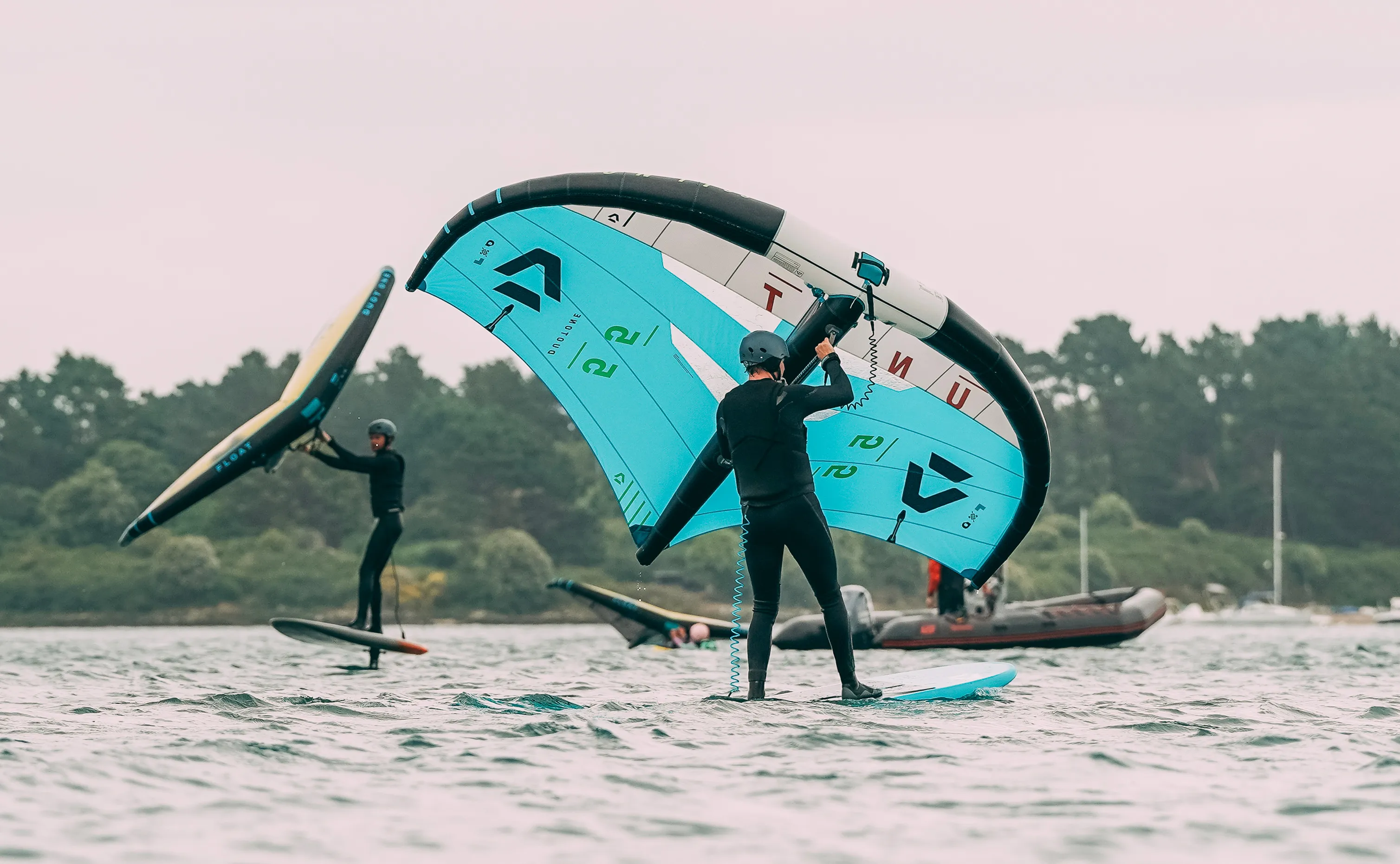 Un cours de wingfoil avec 3 élèves et le montieur sur un bateau en arrière plan