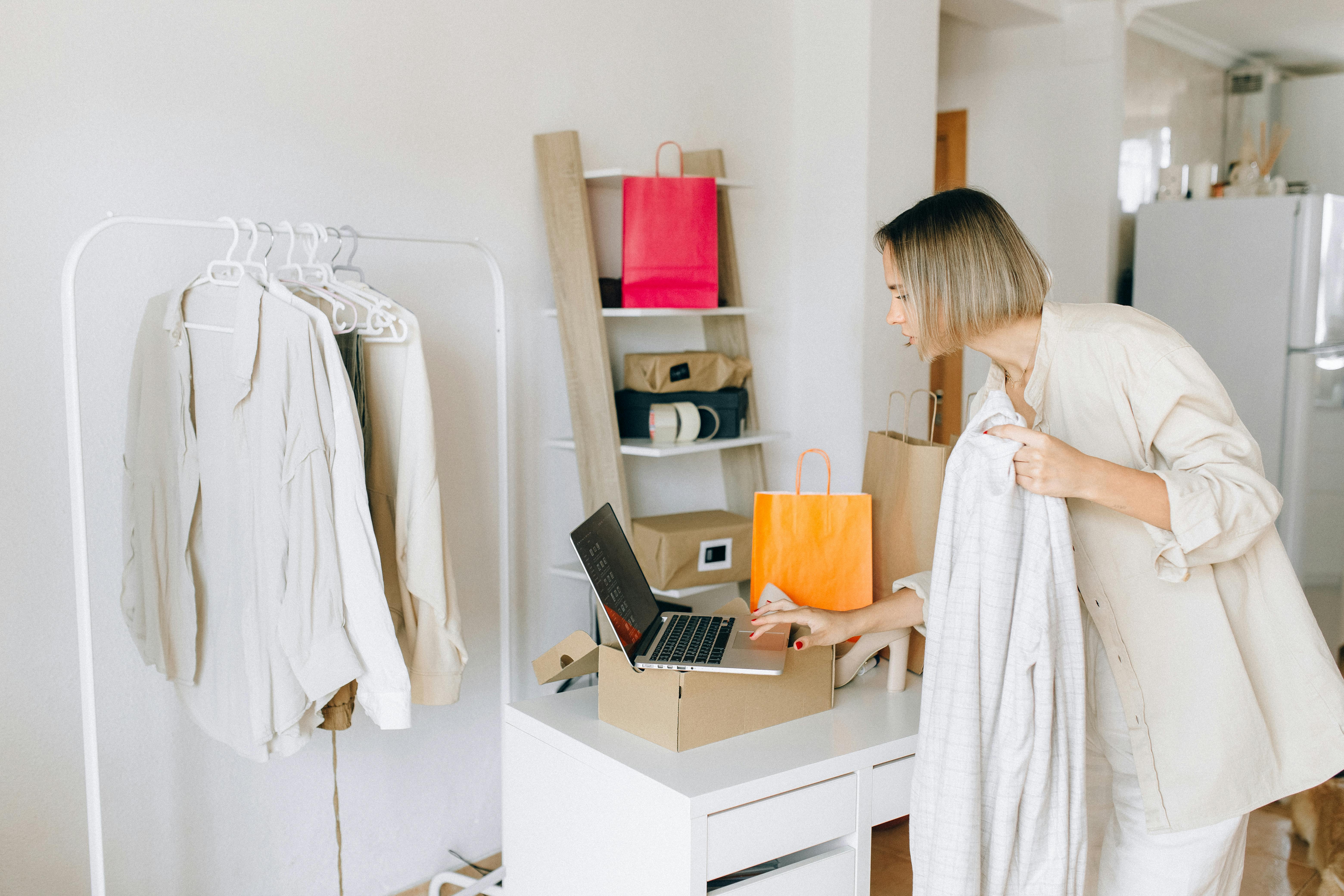 Donna che osserva un capo di abbigliamento davanti al laptop in un ambiente domestico, simbolo di e-commerce, fashion digitale e gestione indipendente.